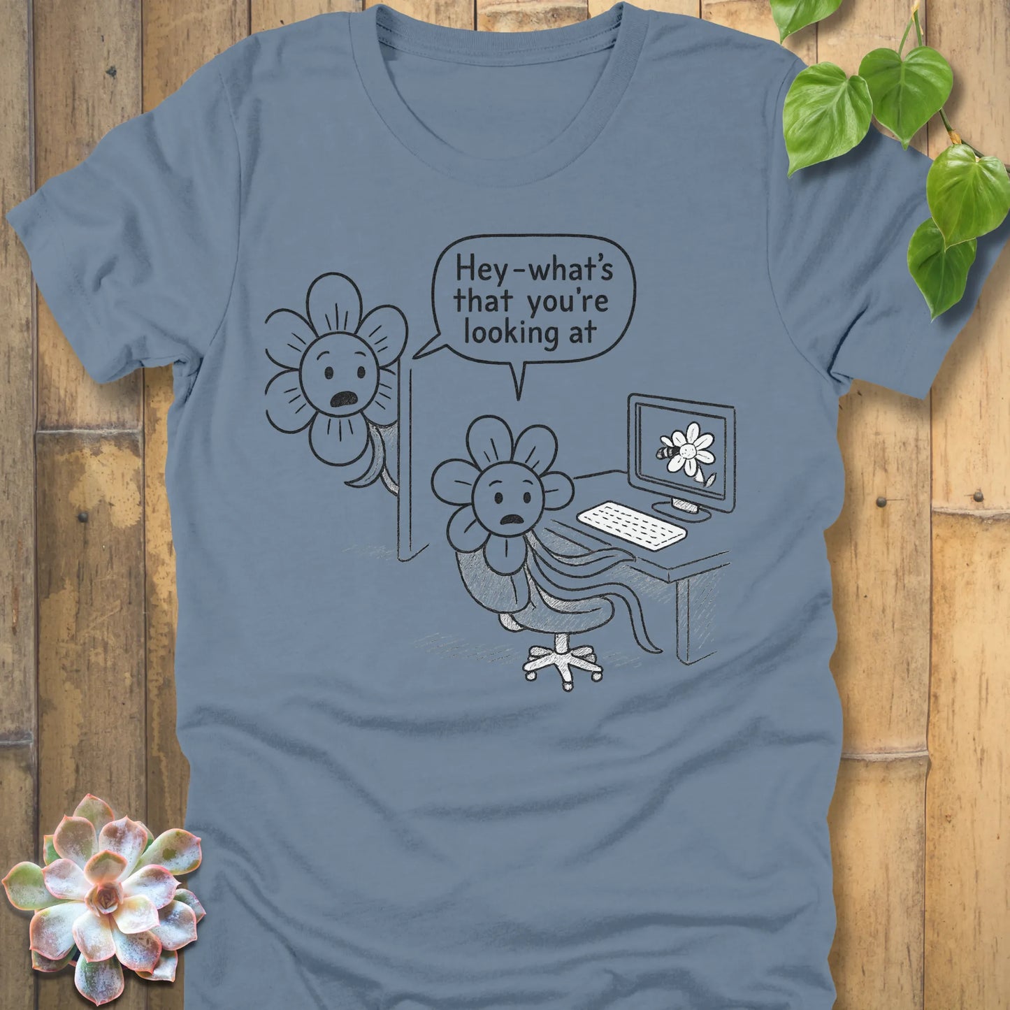 Steel blue Bella+Canvas 3001 T-shirt with a quirky black line comic of two flowers. The first flower sits at a desk, looking at a flower picture on the computer screen. A second flower leans in from the side and asks, ‘Hey—what’s that you’re looking at?