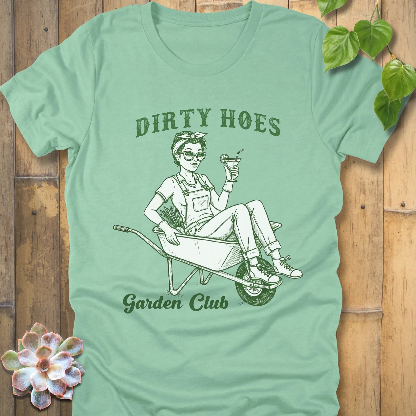Heather Mint t-shirt featuring the design Dirty Hoes, Garden Club printed in green letters with a girl in the trolley, gardening graphic tee.