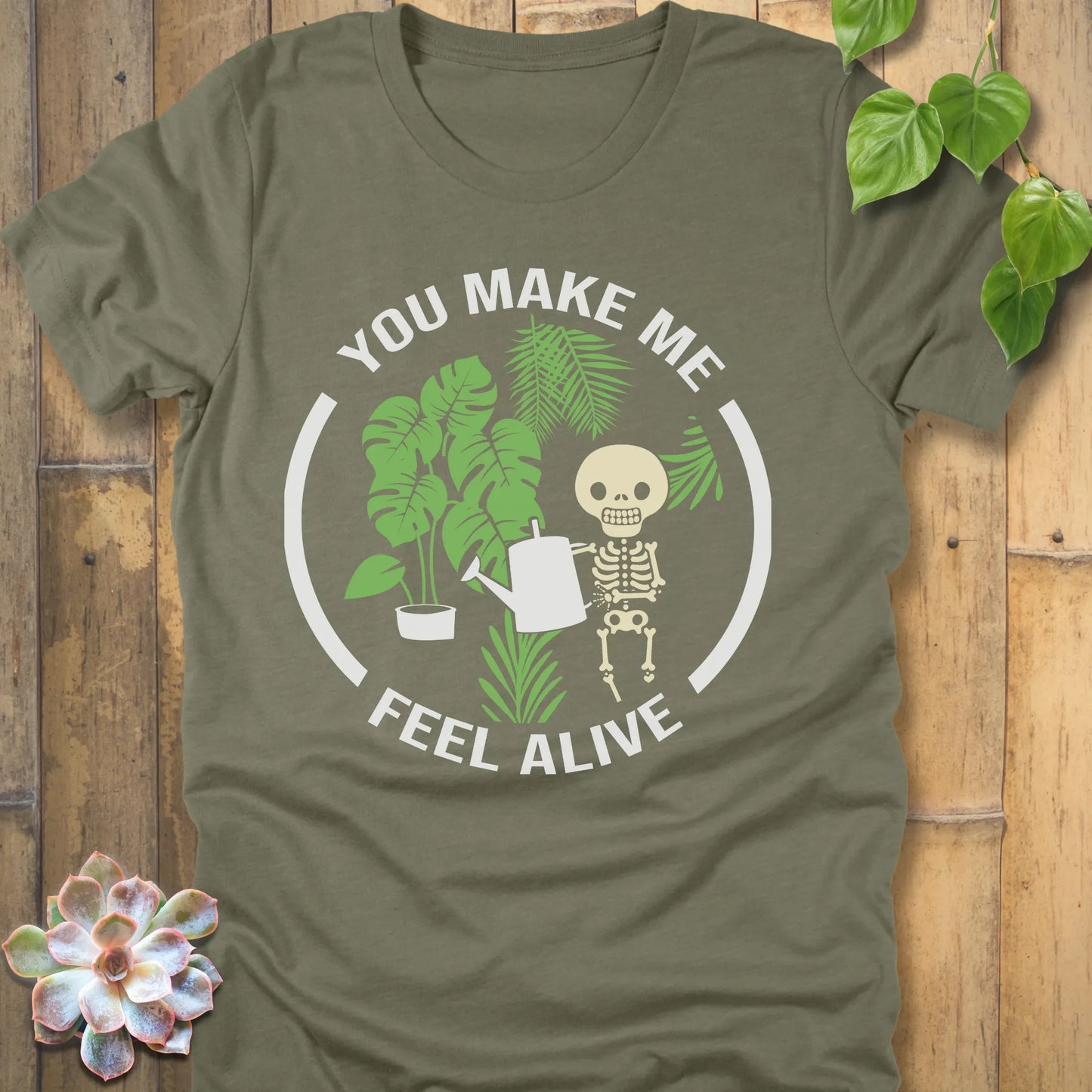 Heather Olive t-shirt featuring the design You make me feel alive with plant and skeleton in bold white letters