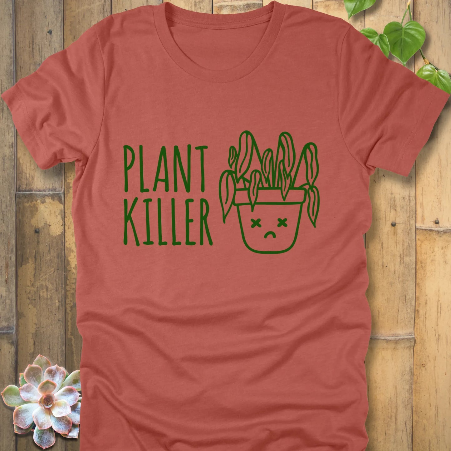 Heather clay t-shirt featuring the design Plant Killer printed in green letters with a plant in an emoji pot