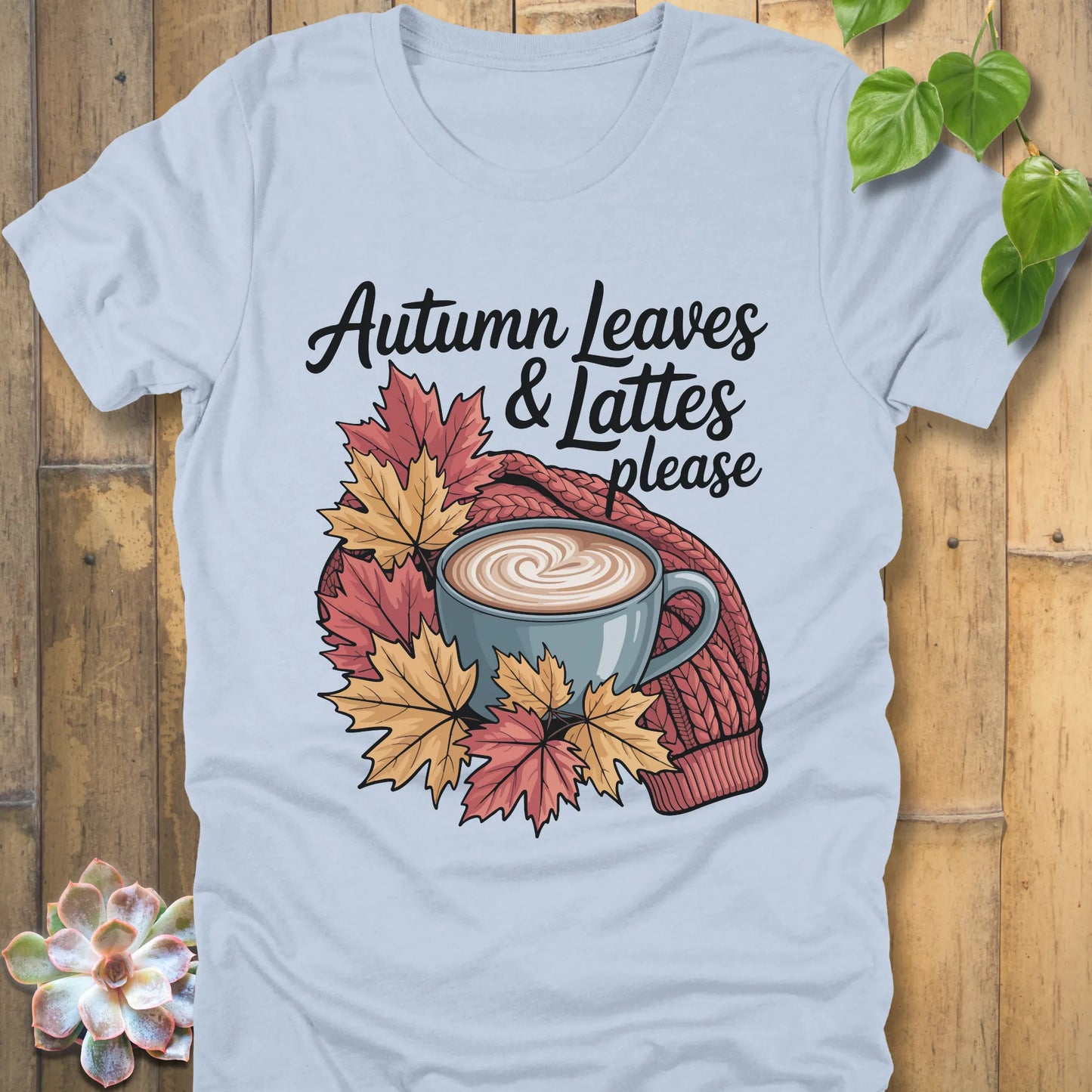 Light blue t-shirt featuring the design Autumn Leaves & Lattes printed in black letters with a mug of coffee and leaves