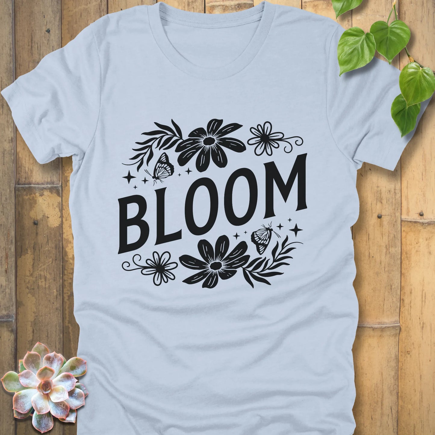 Light blue t-shirt featuring the design " Bloom " printed in bold black letters with flowers