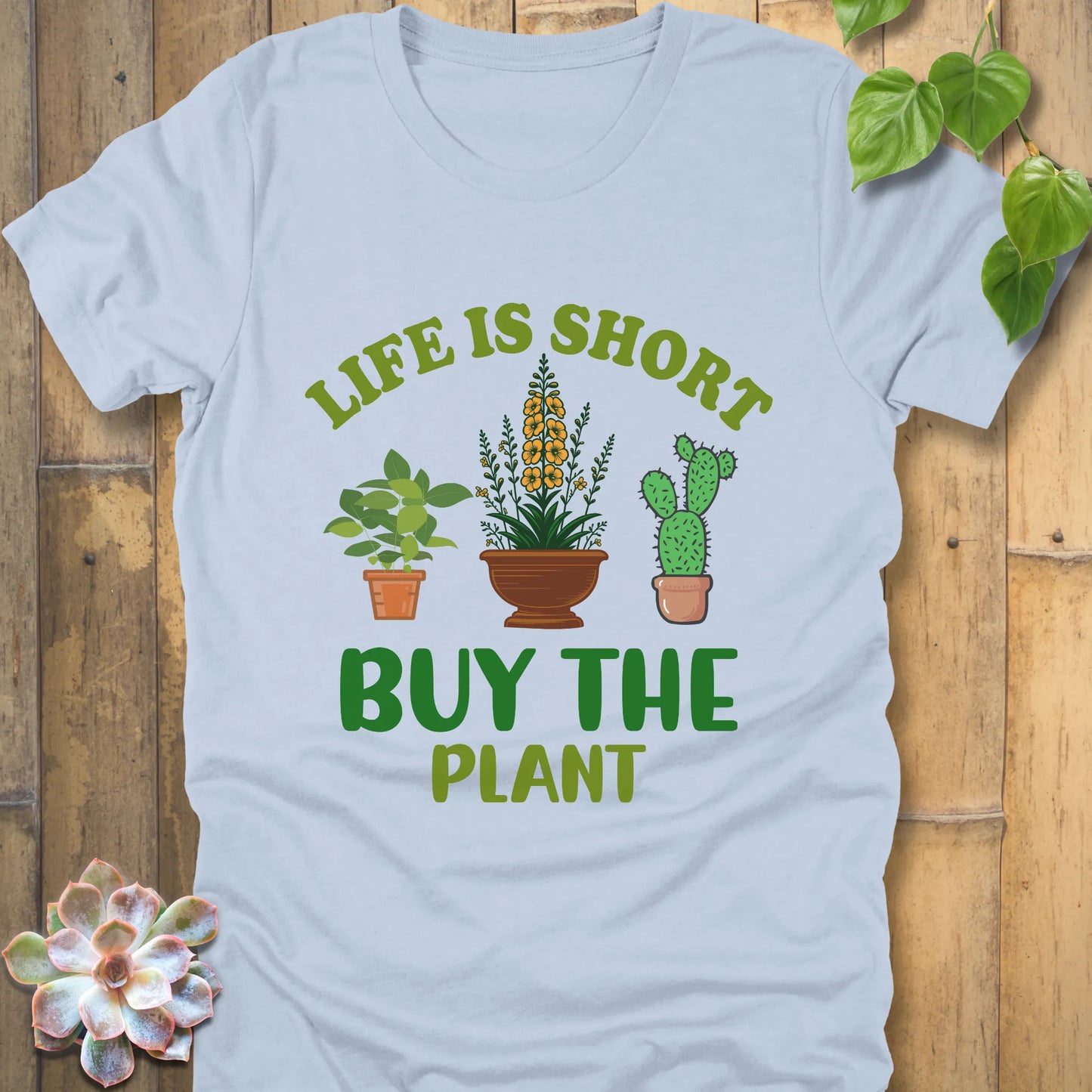 Light blue t-shirt featuring the design Life is short, buy the plant printed in green text with plant illustration