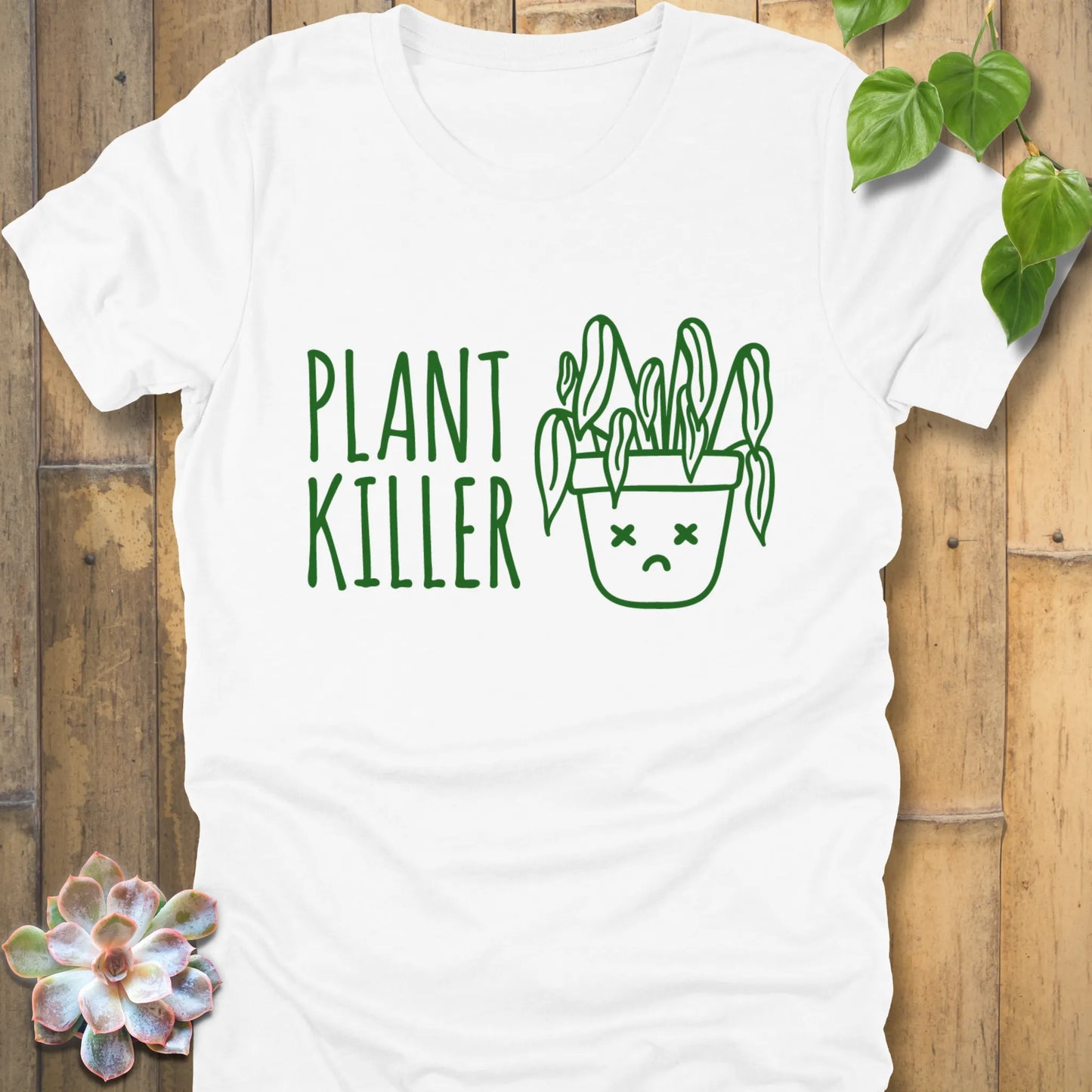 White t-shirt featuring the design Plant Killer printed in green letters with a plant in an emoji pot