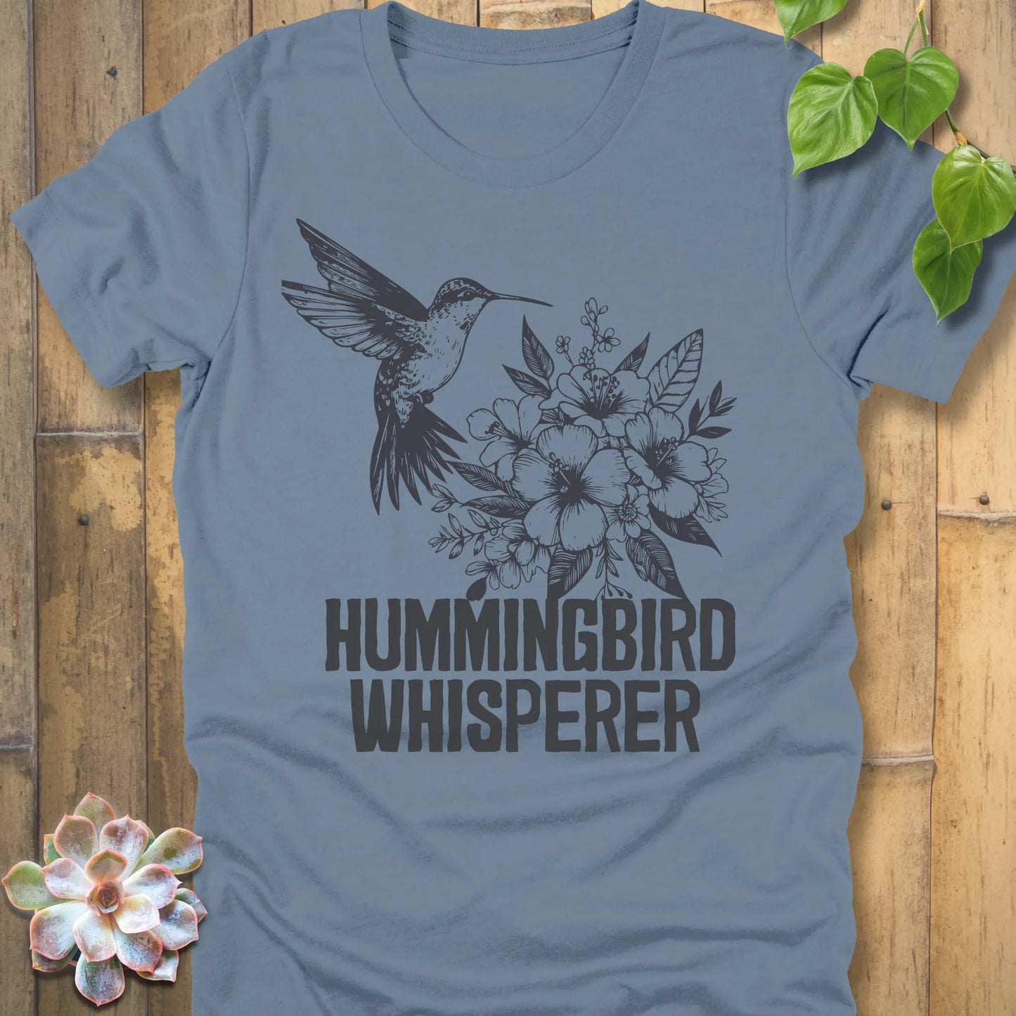 Steel blue “Hummingbird Whisperer” T-shirt with a minimalist black hummingbird and flowers illustration, perfect for gardeners and wildlife enthusiasts