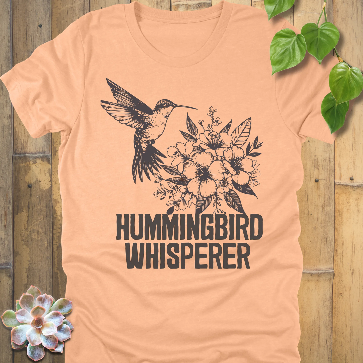 Heather peach “Hummingbird Whisperer” graphic tee showing a hummingbird and floral bouquet in black ink, lightweight comfortable shirt for bird lovers