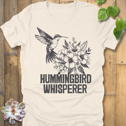 Natural off-white “Hummingbird Whisperer” T-shirt with black hummingbird and floral artwork, eco-toned garden lover’s graphic shirt.