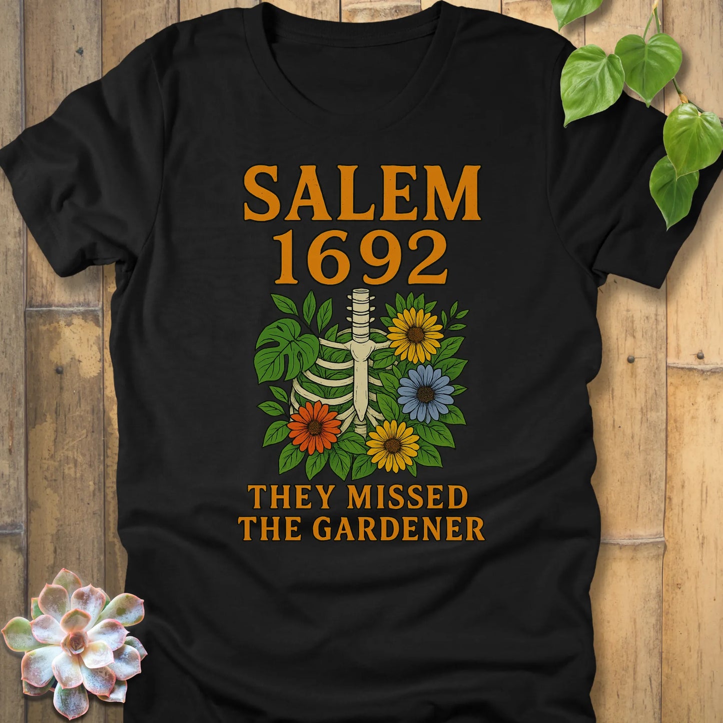 Heather Black – Salem 1692 They Missed the Gardener T-shirt in Black, bold orange text and floral skeleton print, Bella+Canvas cotton tee.
