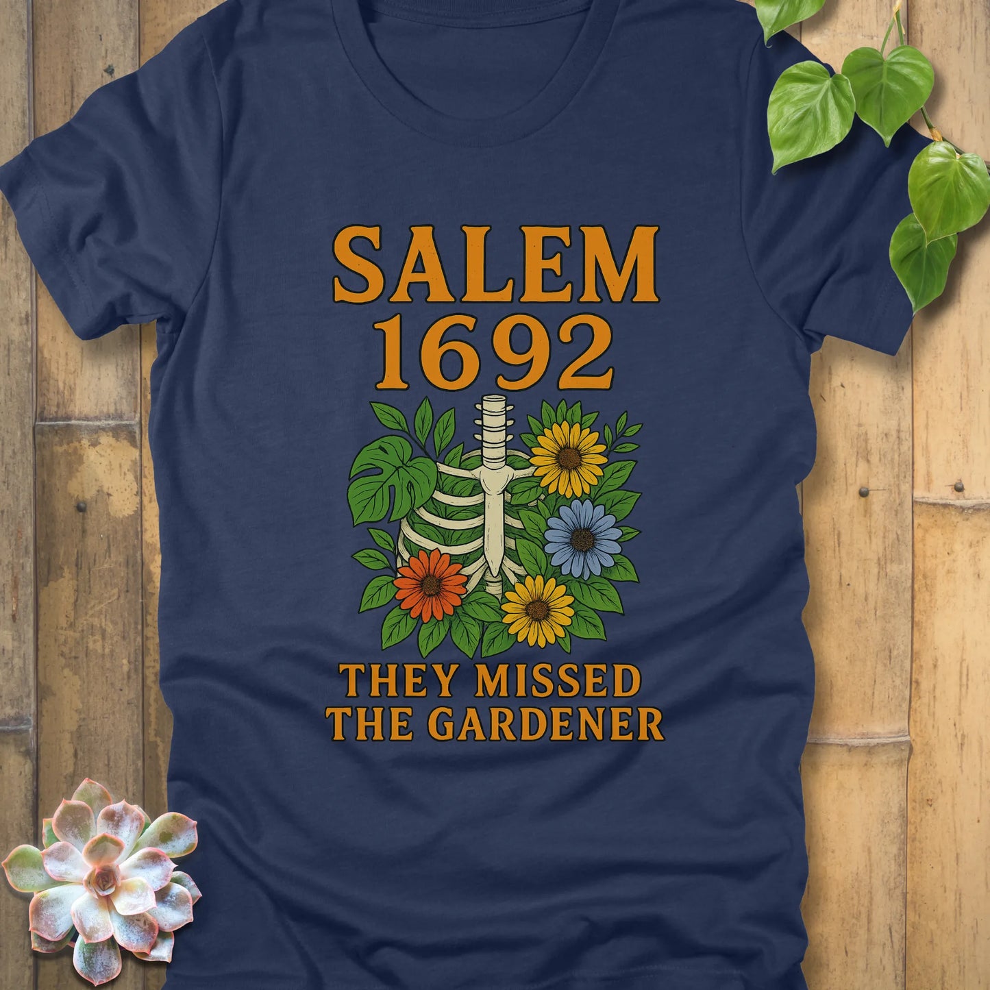 Heather Navy – Salem 1692 They Missed the Gardener T-shirt in Navy, orange text with floral ribcage design, unisex Bella+Canvas tee.