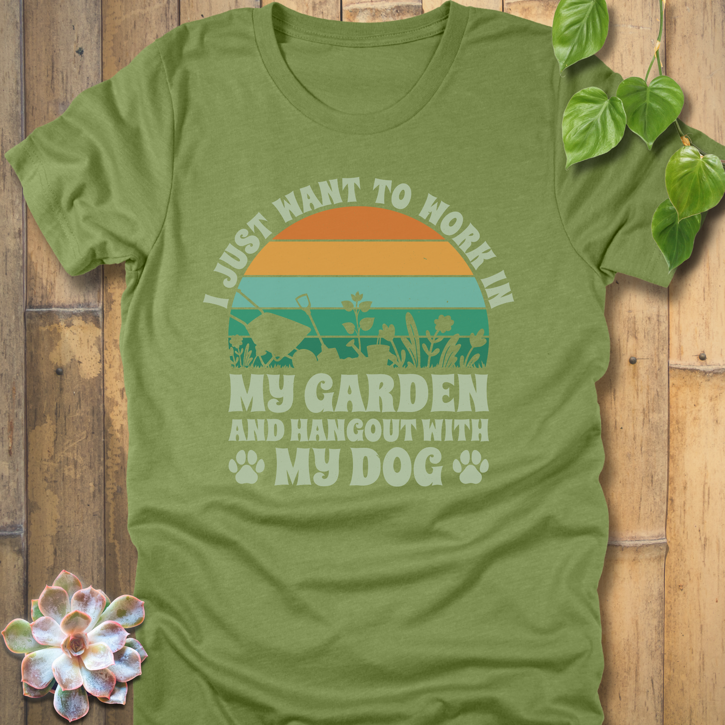 Heather Green t-shirt with a retro orange and teal sunset, garden tool silhouettes, and slogan text saying I just want to work in my garden and hang out with my dog