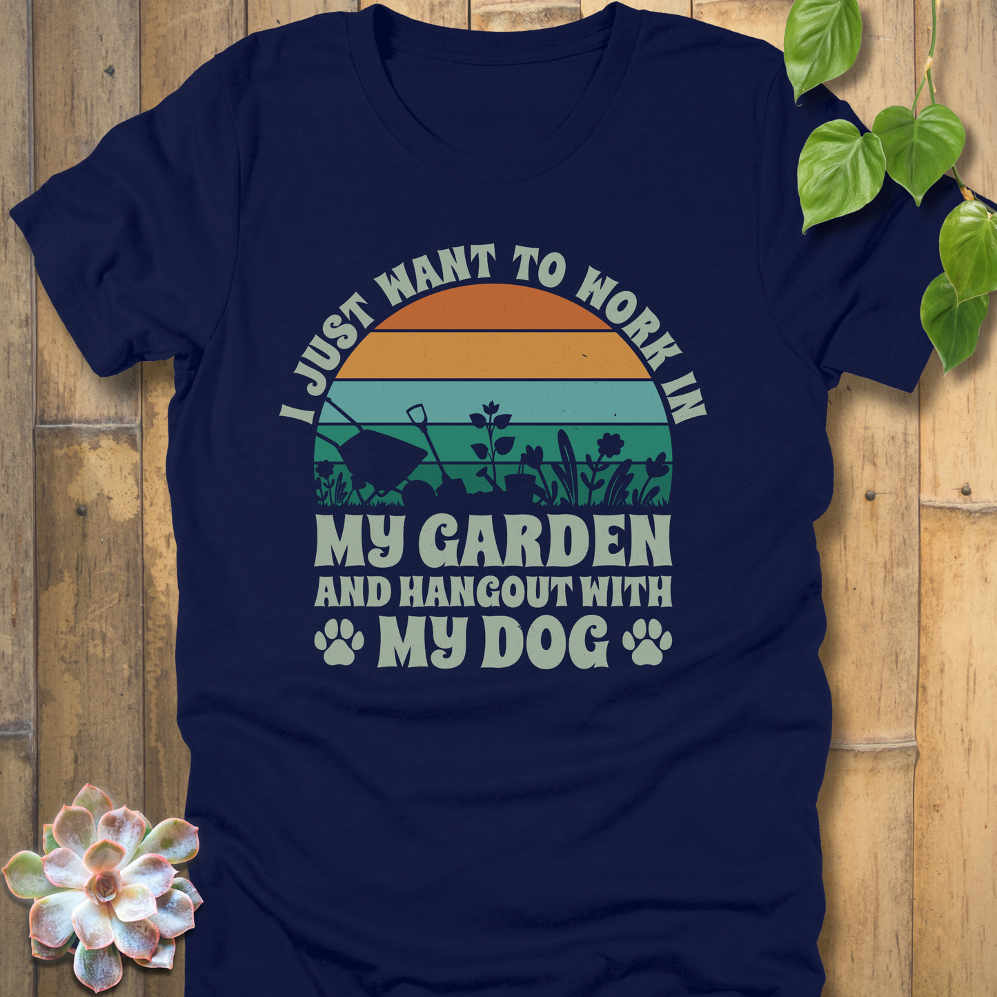 Heather Navy graphic tee showing a colourful retro sunset, garden tools, plants, paw prints, and the phrase I just want to work in my garden and hang out with my dog