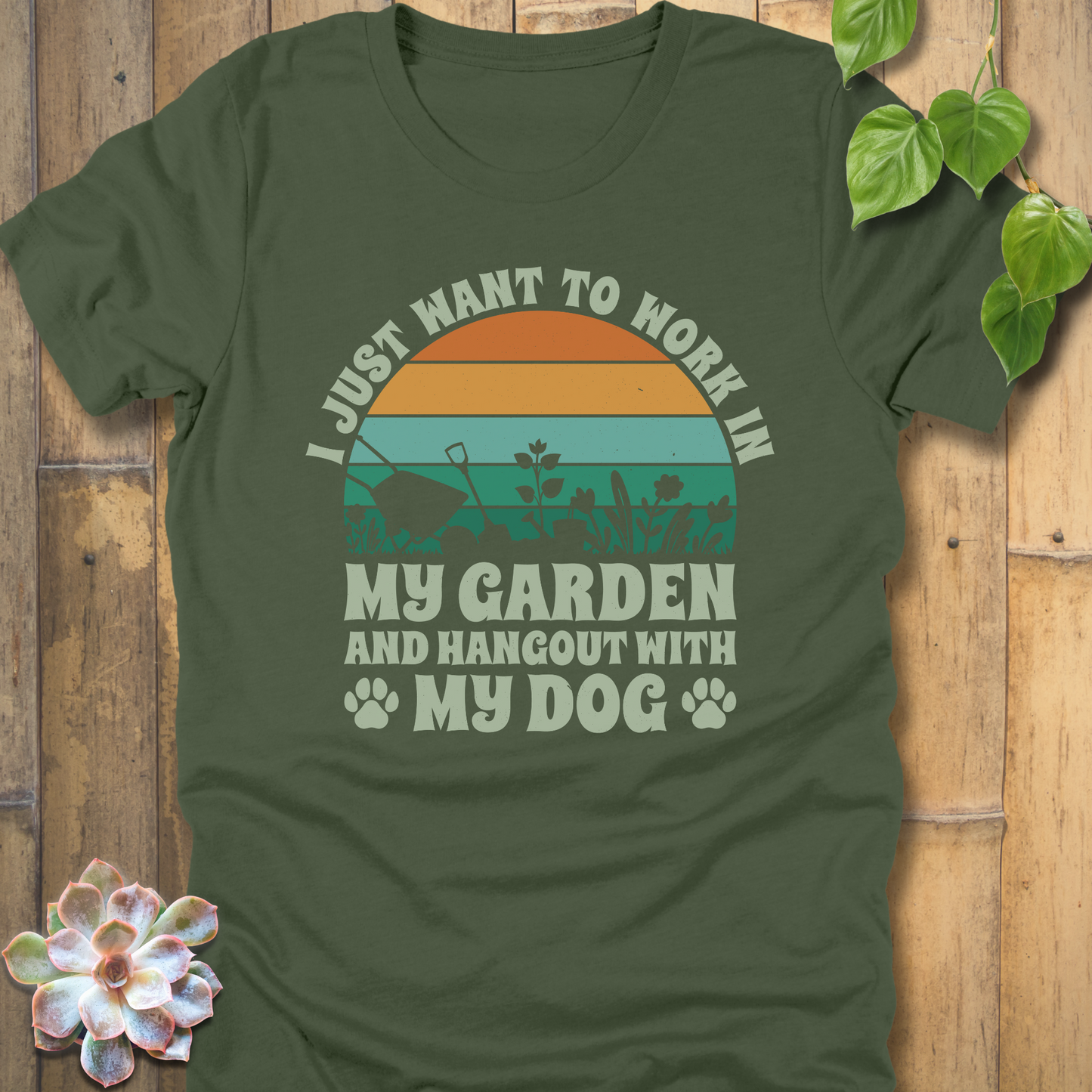 Military Green novelty t-shirt featuring a retro sunset with orange and teal stripes, garden tools and plants, and text saying I just want to work in my garden and hang out with my dog