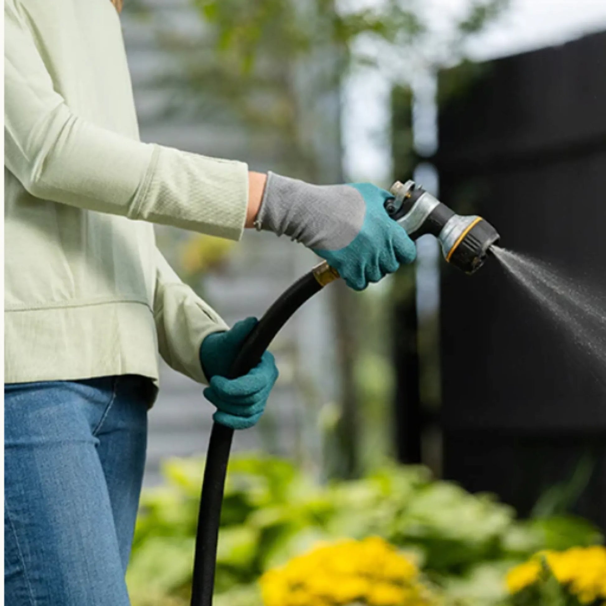 Water-resistant turquoise gardening gloves with floral backing in use while watering plants with a hose