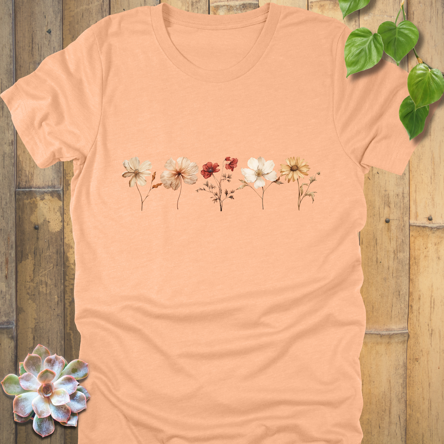 Heather Peach t-shirt featuring a horizontal arrangement of dried wildflowers in natural cream, orange, and red hues