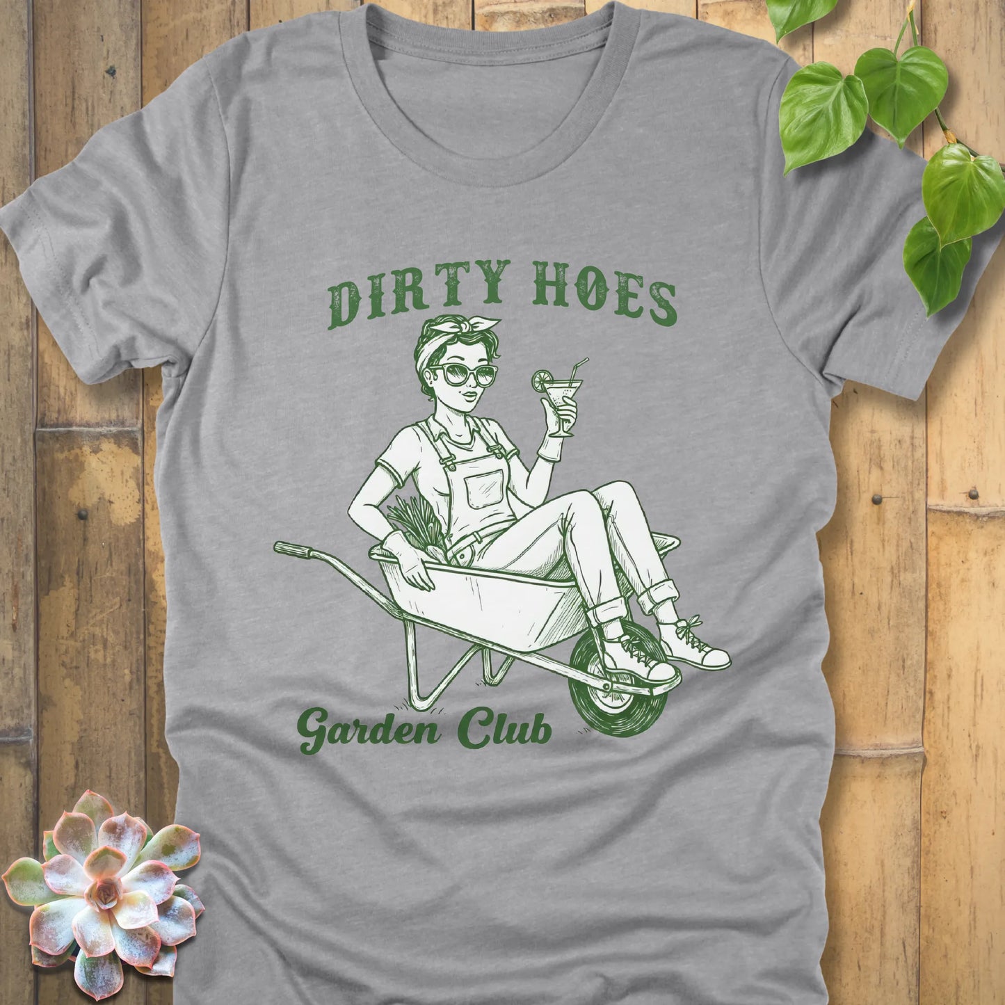Athletic Heather t-shirt featuring the design Dirty Hoes, Garden Club printed in green letters with a girl in the trolley, gardening graphic tee.