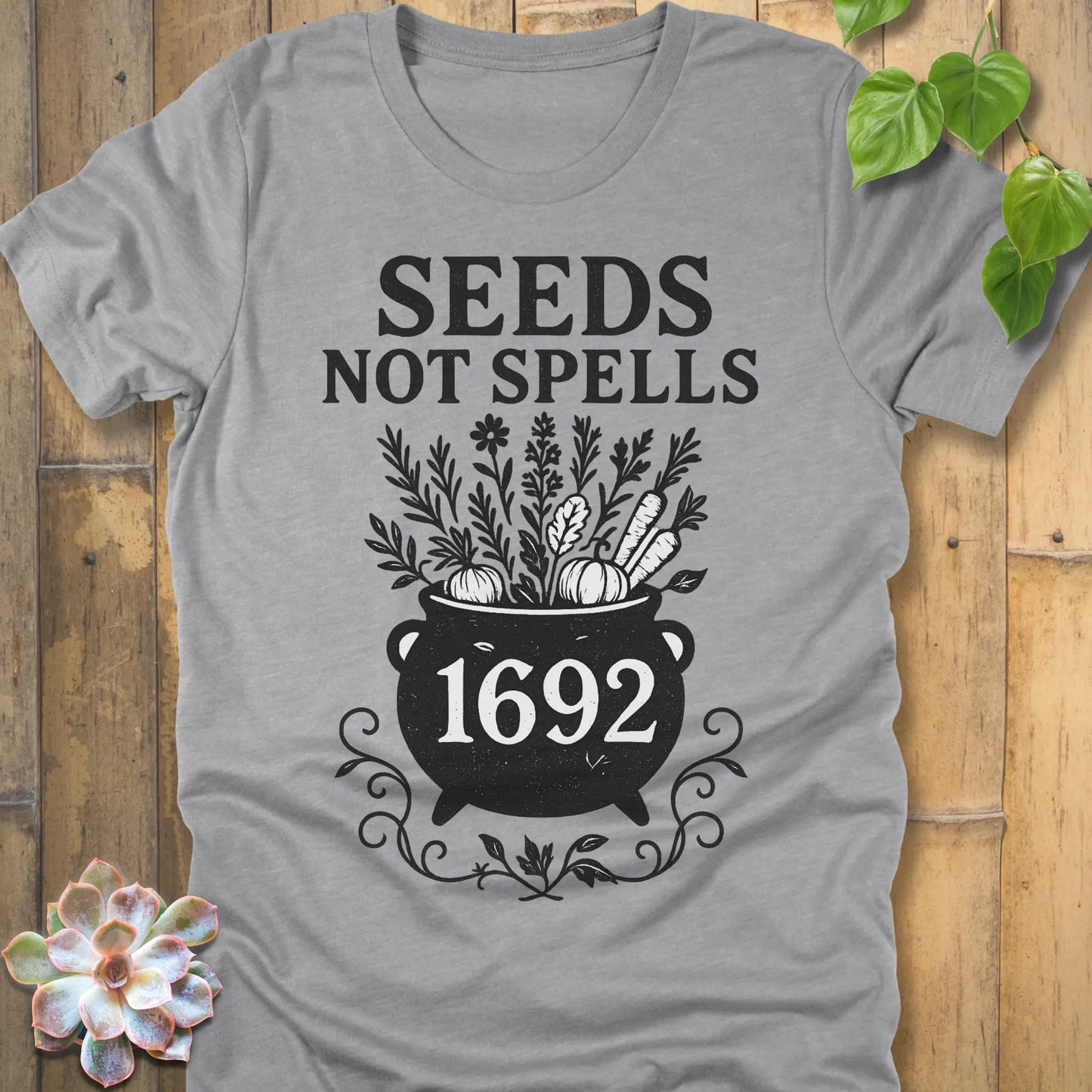 Athletic Heather t-shirt featuring the design Seeds Not Spells printed in bold black letters, halloween gardening graphic tee.