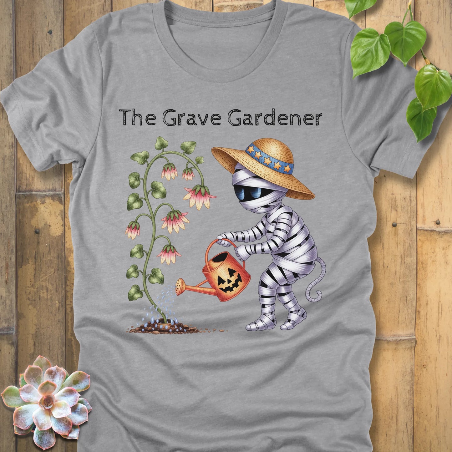 Athletic Heather t-shirt featuring the design The Grave Gardener printed in bold black letters and a ghost watering the plant