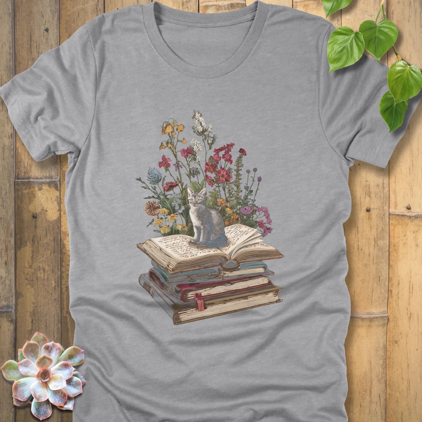 Athletic Heather t-shirt featuring the design Whiskers & Words with a cat sitting on books and flowers, eco-style tee for book and cat lovers.