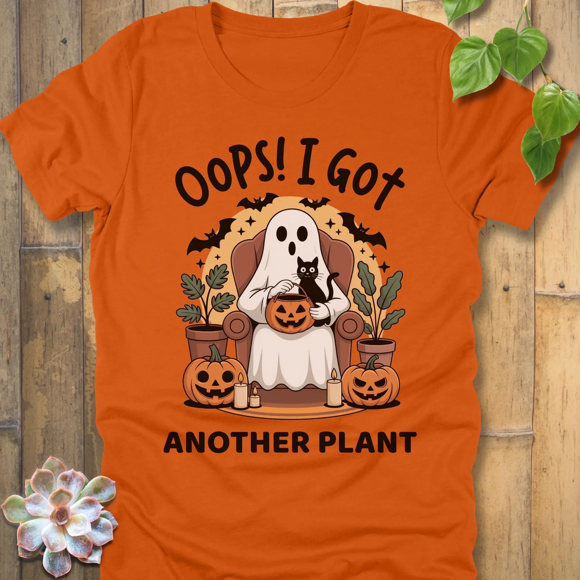 Autumn t-shirt featuring the design "Oops! I Got Another Plant" printed in bold black letters, and a ghost, cat, plants, bats and pumpkin