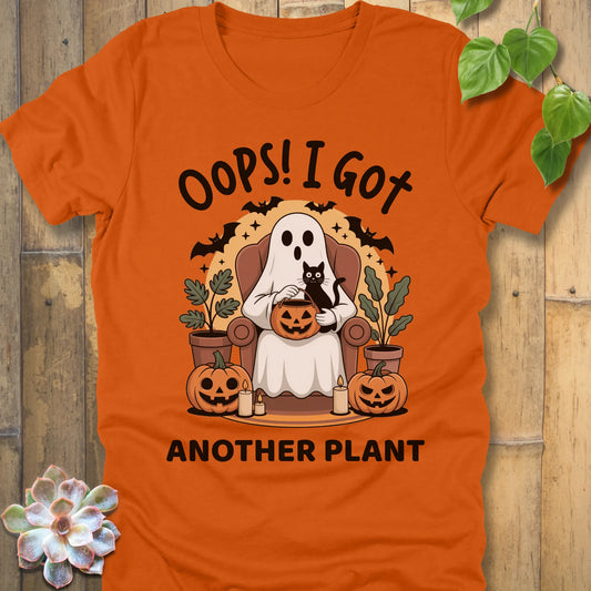 Autumn t-shirt featuring the design "Oops! I Got Another Plant" printed in bold black letters, and a ghost, cat, plants, bats and pumpkin