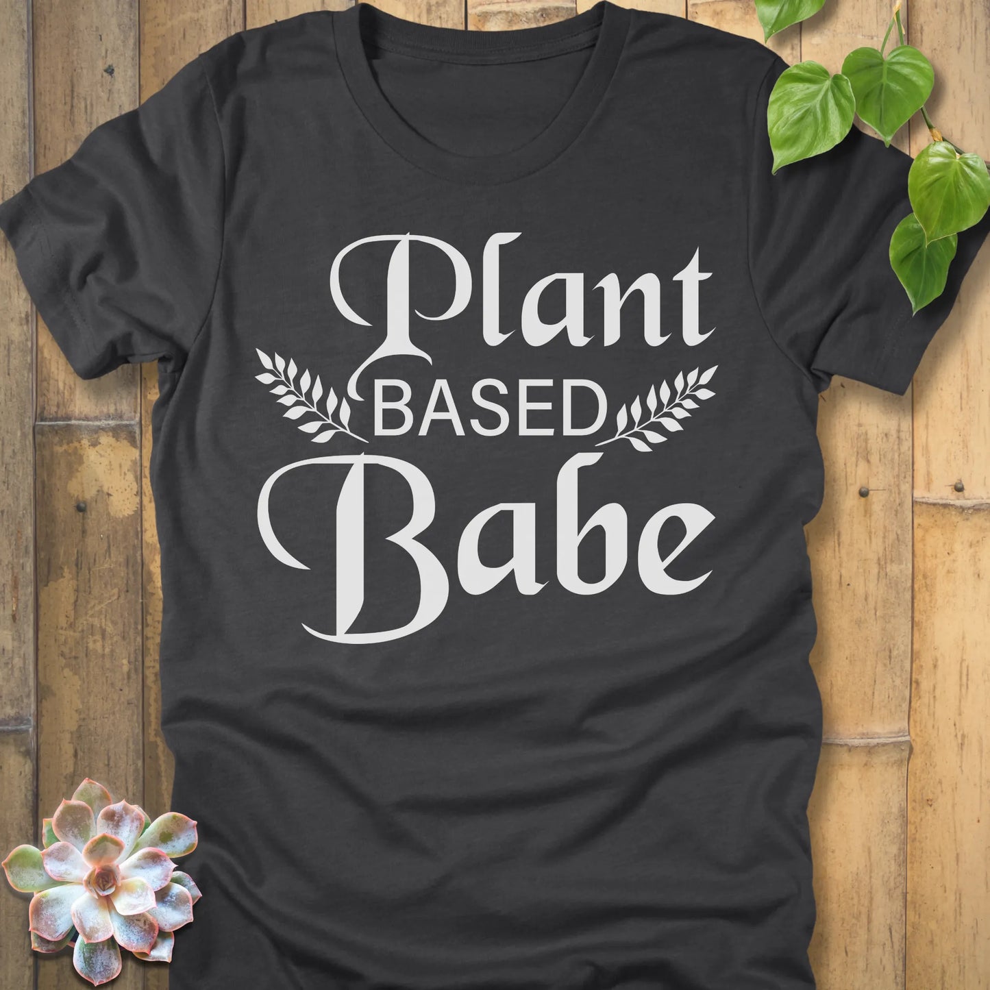 Dark Grey Heather t-shirt featuring the design Plant Based Babe printed in bold letters and a graphic leaves, vegan lifestyle shirt.