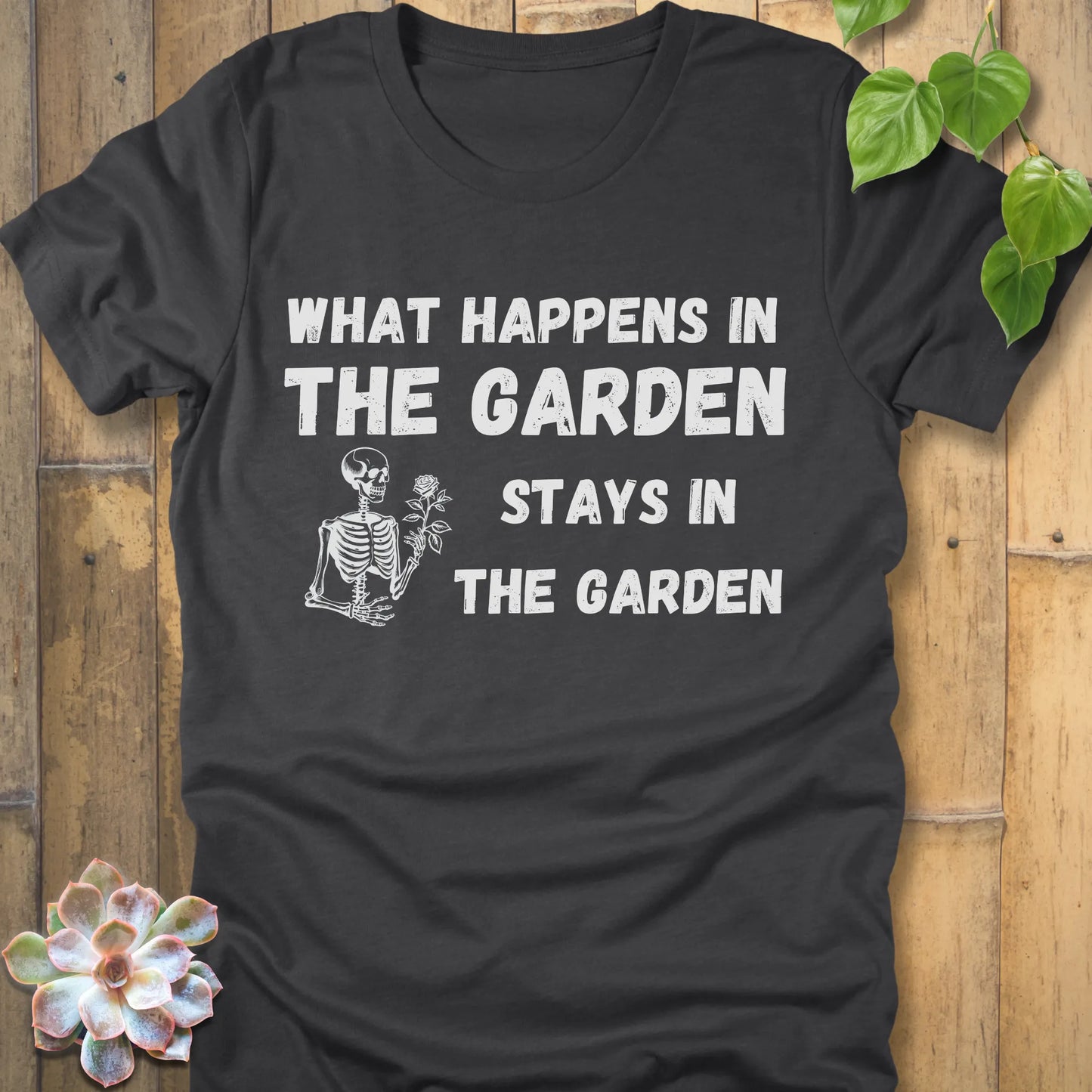 Dark Grey Heather t-shirt featuring the design What Happens In The Garden Stays In The Garden printed in bold letters with skeleton and flower
