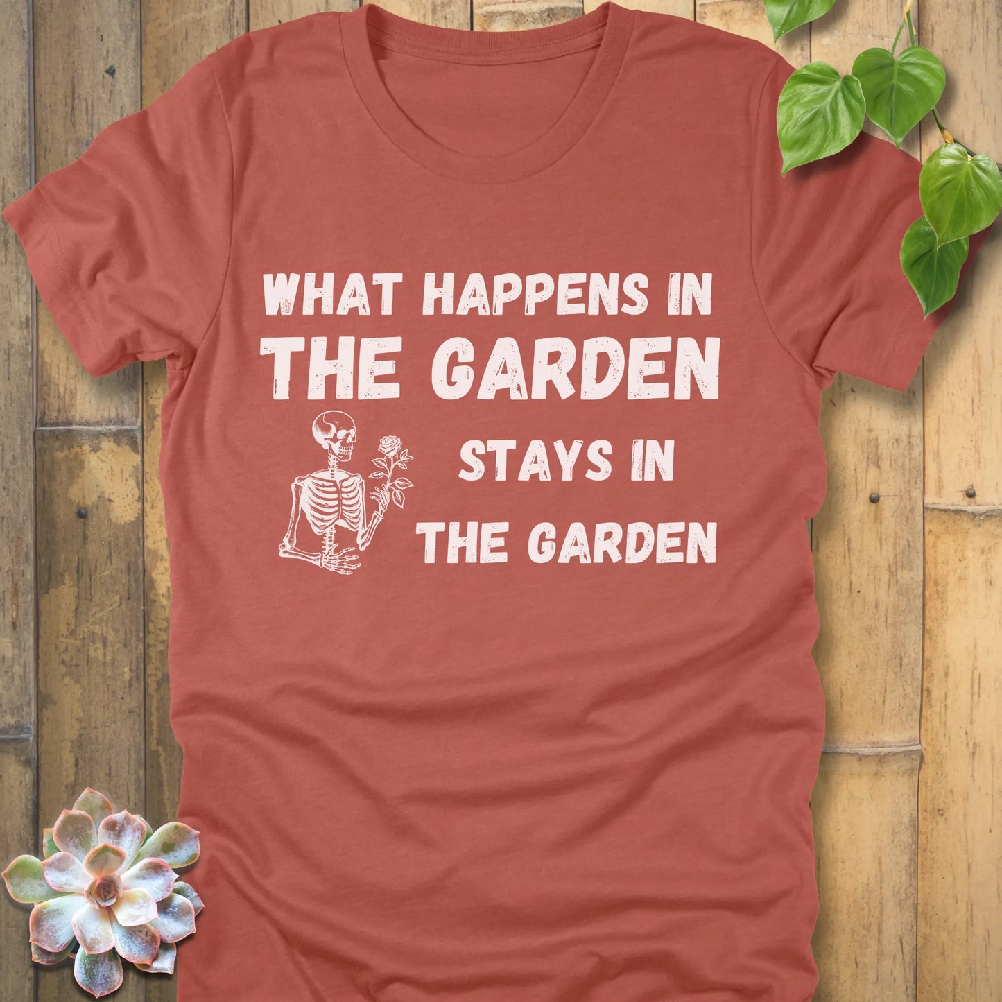 Heather Clay t-shirt featuring the design What Happens In The Garden Stays In The Garden printed in bold letters with skeleton and flower