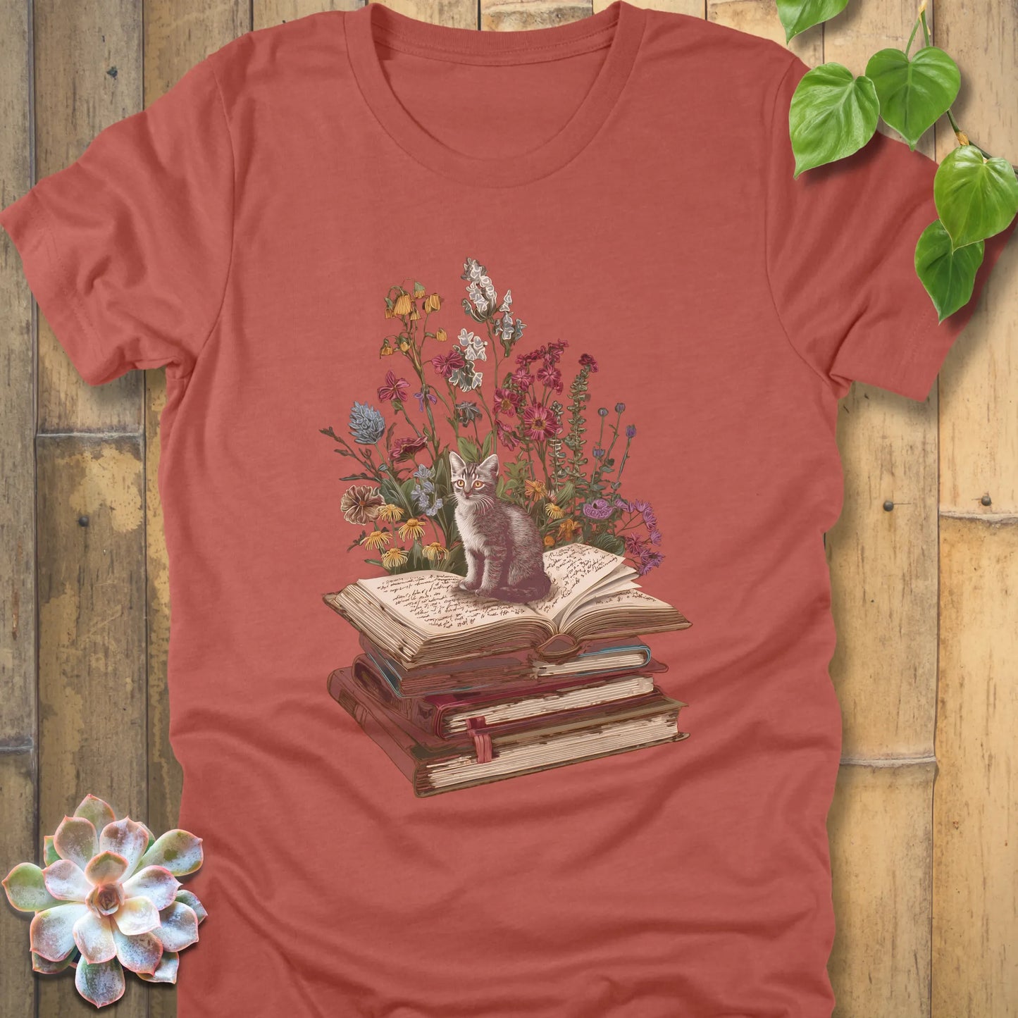 Heather Clay t-shirt featuring the design Whiskers & Words with a cat sitting on books and flowers, eco-style tee for book and cat lovers.