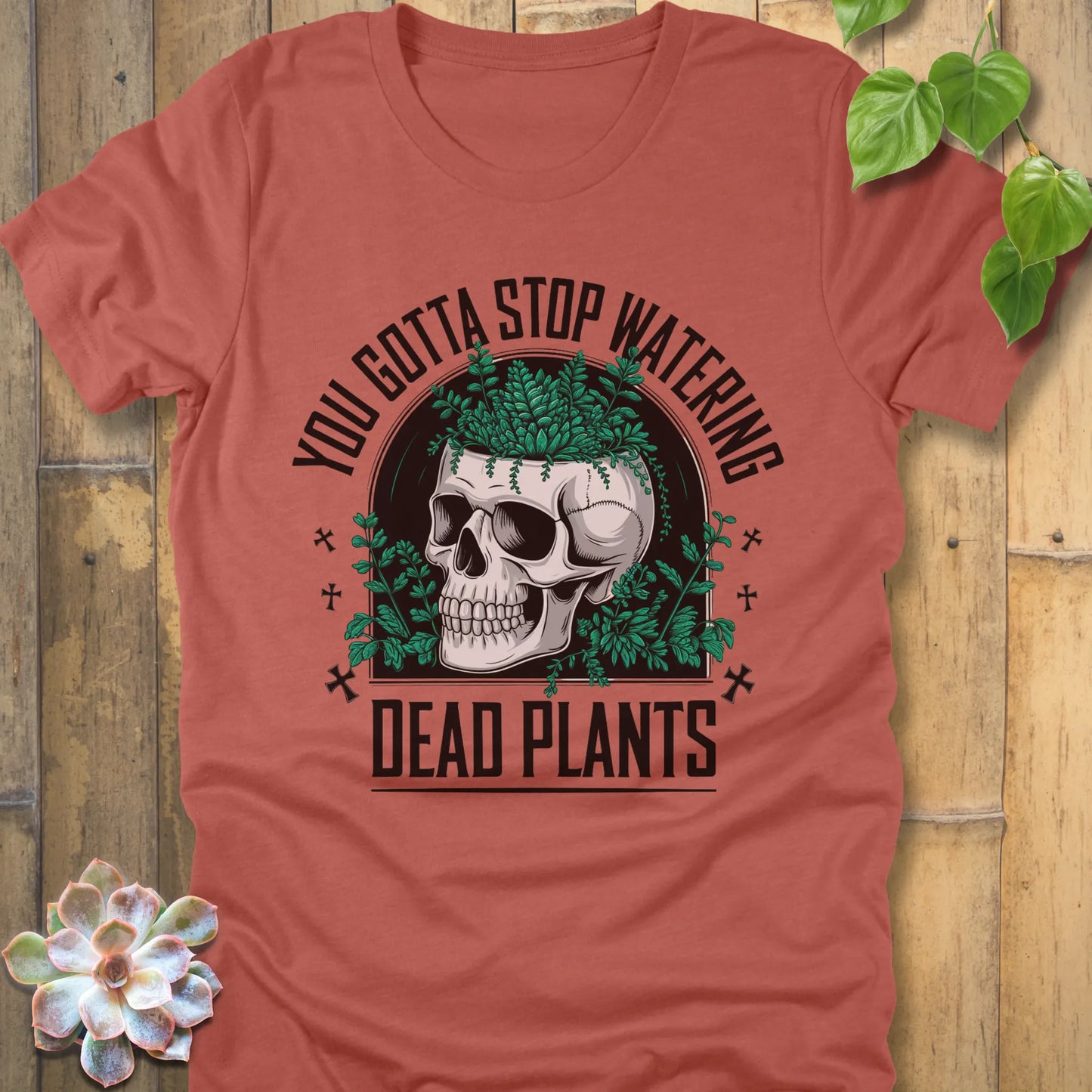 Heather Clay t-shirt featuring the design “You gotta stop watering dead plants” printed in black letters with skull and plants graphic