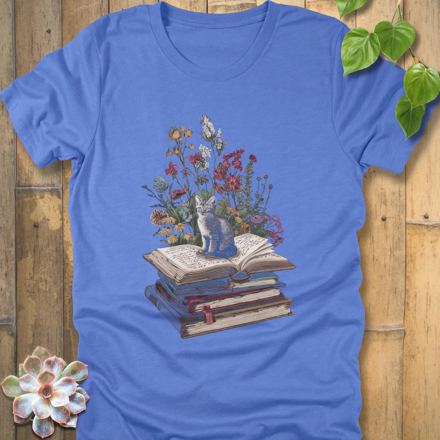 Heather Colombia Blue t-shirt featuring the design Whiskers & Words with a cat sitting on books and flowers, eco-style tee for book and cat lovers.