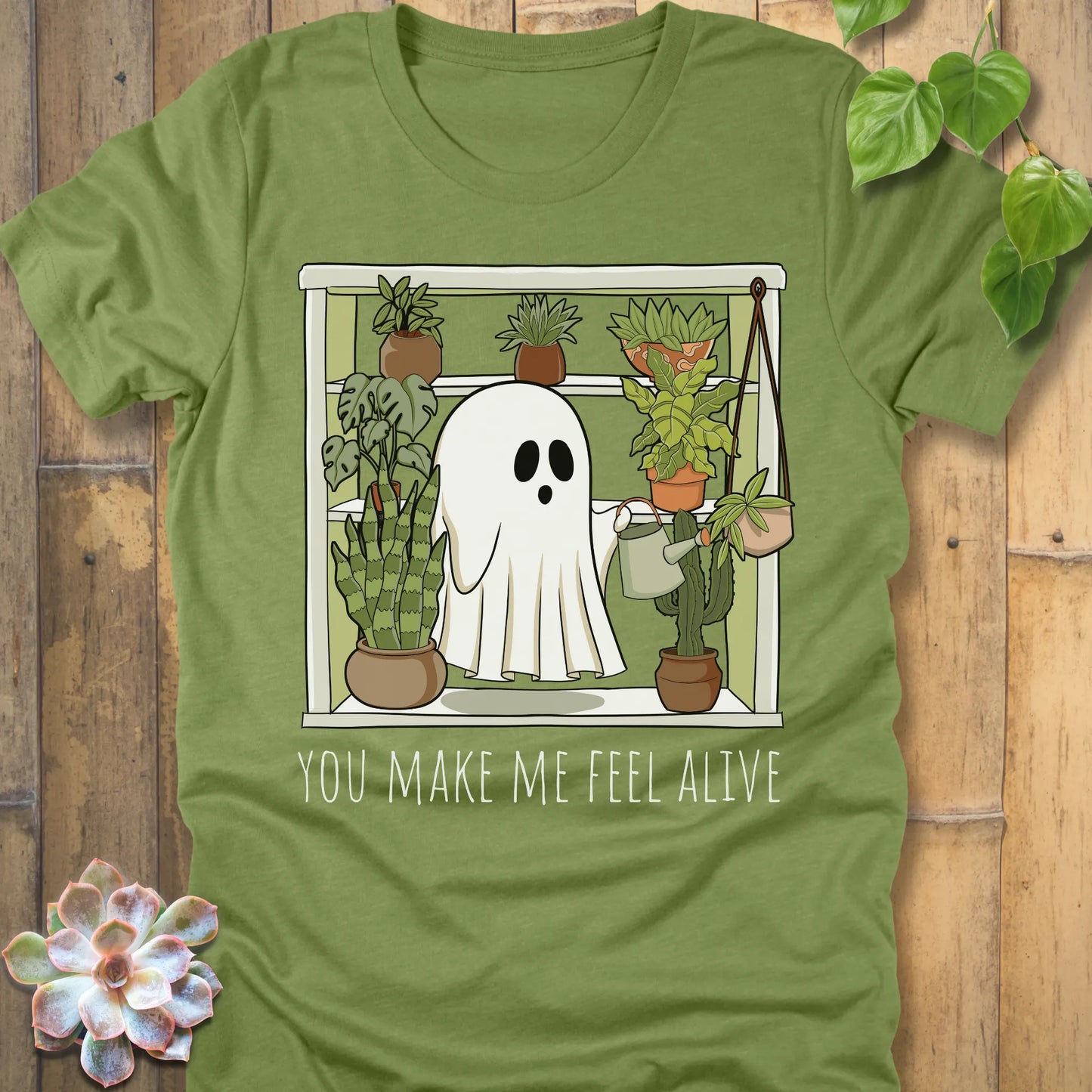Heather Green t-shirt featuring the design Make Me Feel Alive printed in bold white letters and a halloween ghost watering the plants design