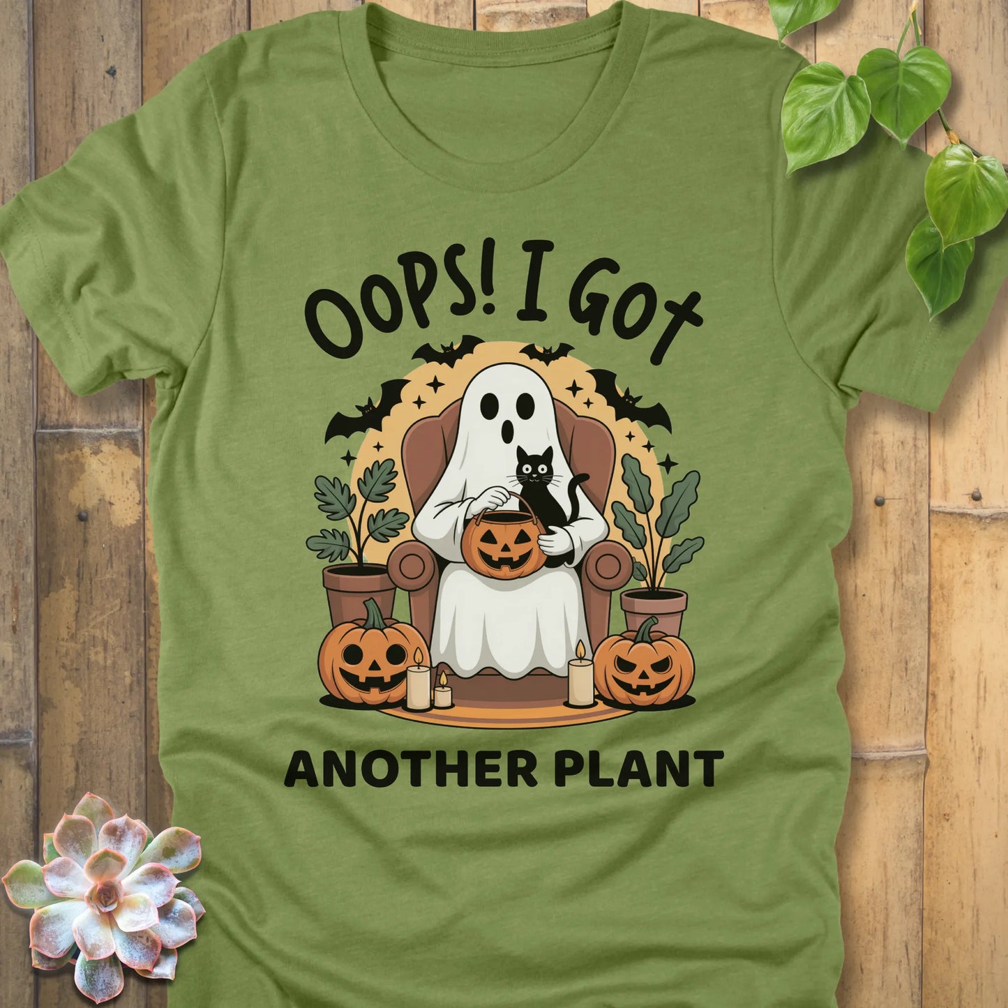 Heather Green t-shirt featuring the design "Oops! I Got Another Plant" printed in bold black letters, and a ghost, cat, plants, bats and pumpkin