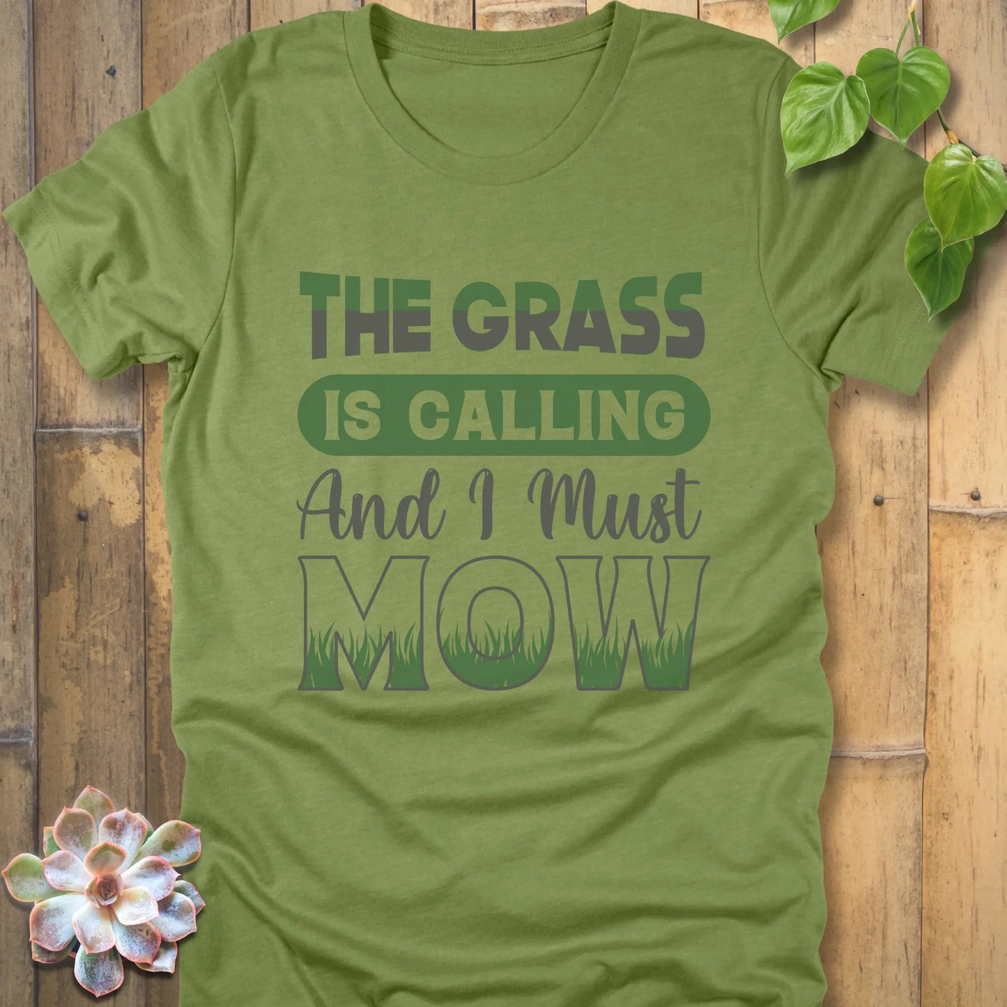 Heather Green t-shirt featuring the design The Grass is Calling and I Must Mow in bold letters and with grass