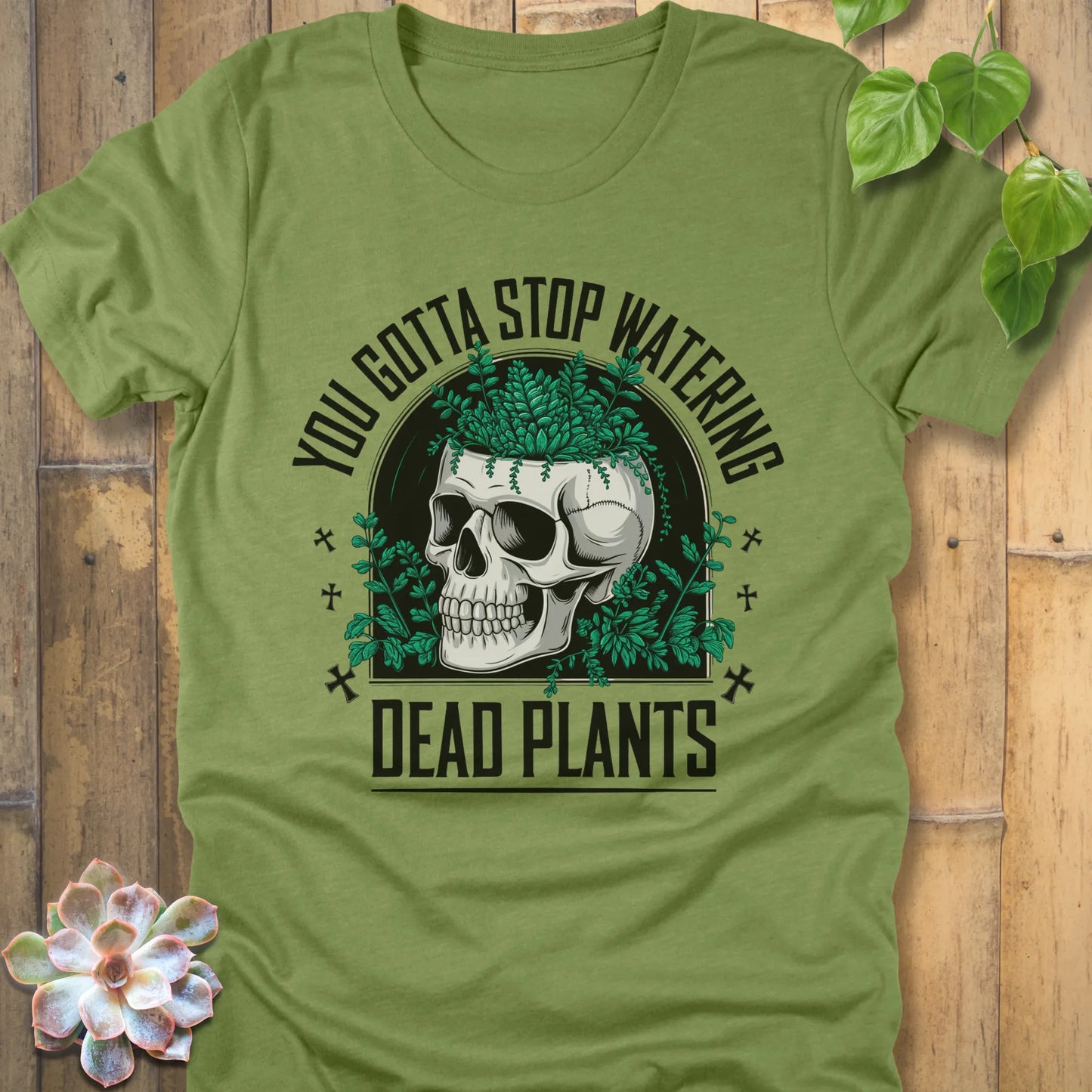 Heather Green t-shirt featuring the design “You gotta stop watering dead plants” printed in black letters with skull and plants graphic