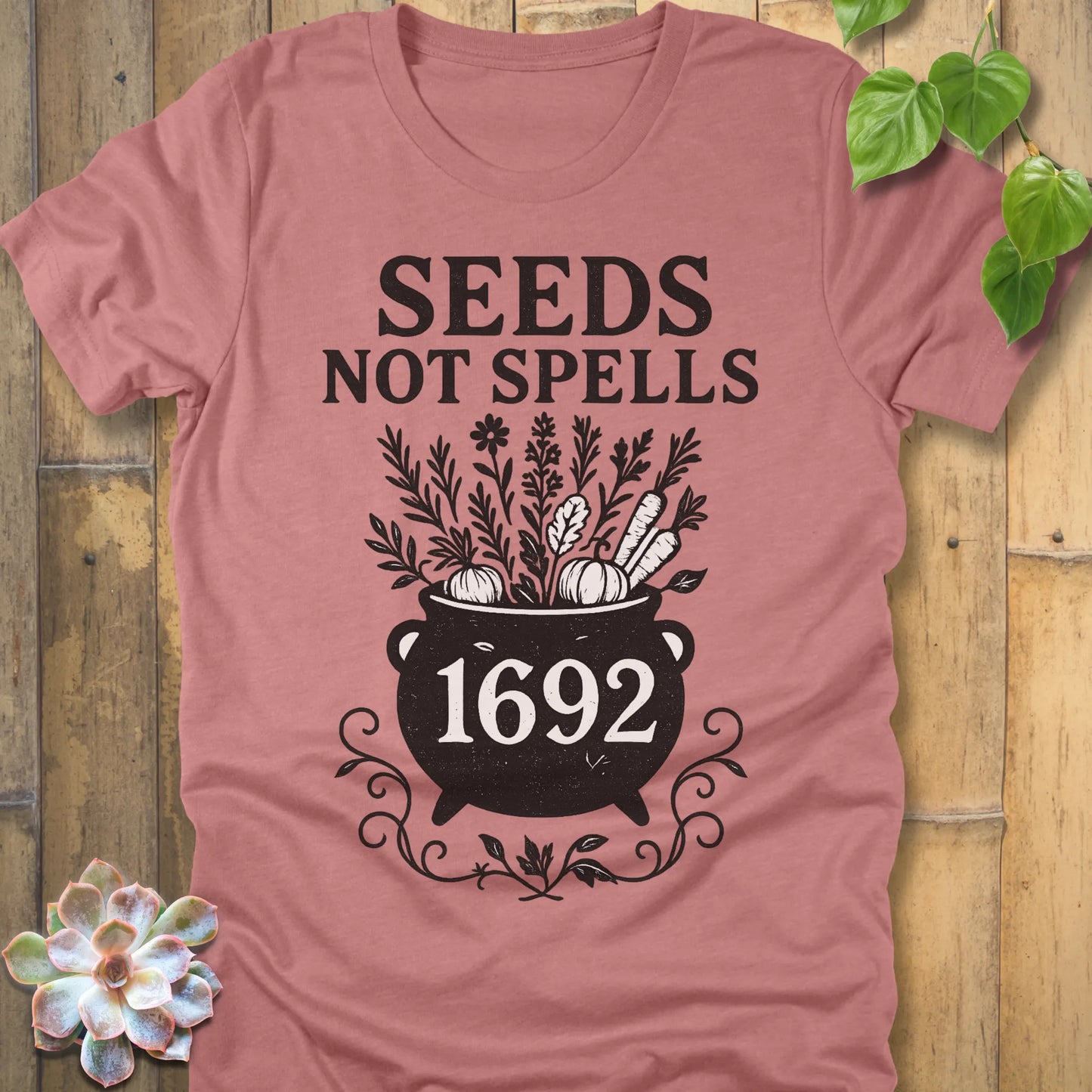 Heather Mauve t-shirt featuring the design Seeds Not Spells printed in bold black letters, halloween gardening graphic tee.