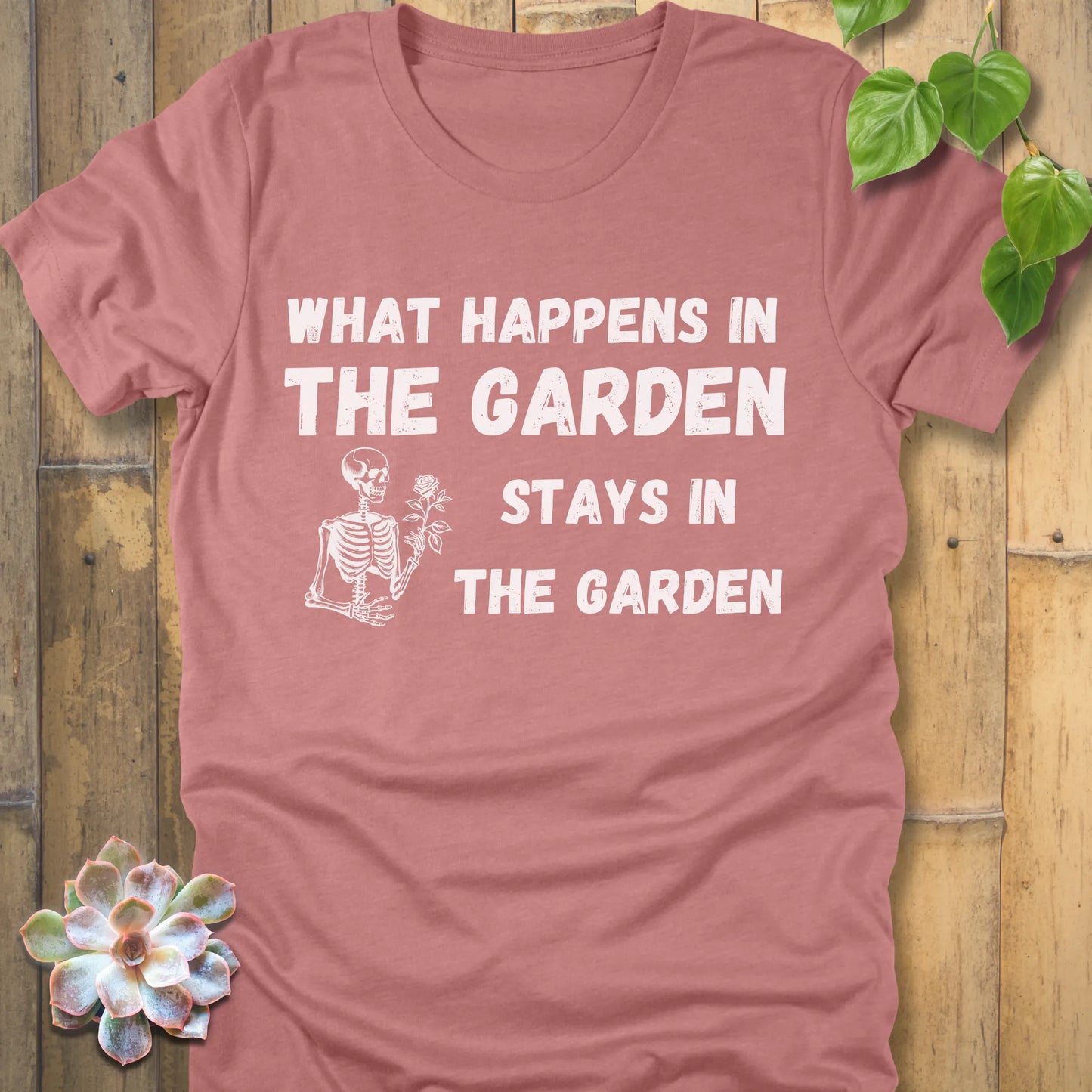 Heather Mauve t-shirt featuring the design What Happens In The Garden Stays In The Garden printed in bold letters with skeleton and flower