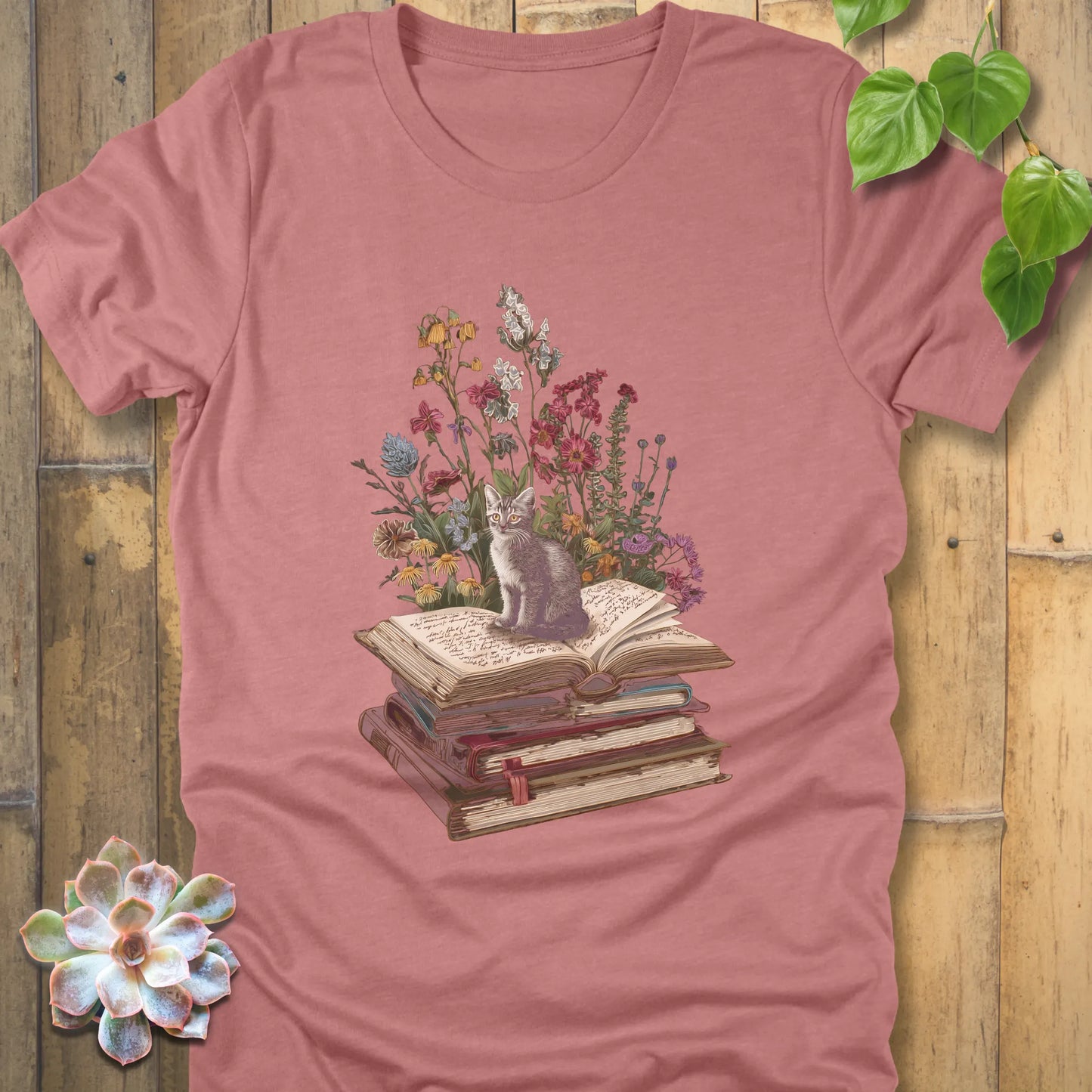 Heather Mauve t-shirt featuring the design Whiskers & Words with a cat sitting on books and flowers, eco-style tee for book and cat lovers.