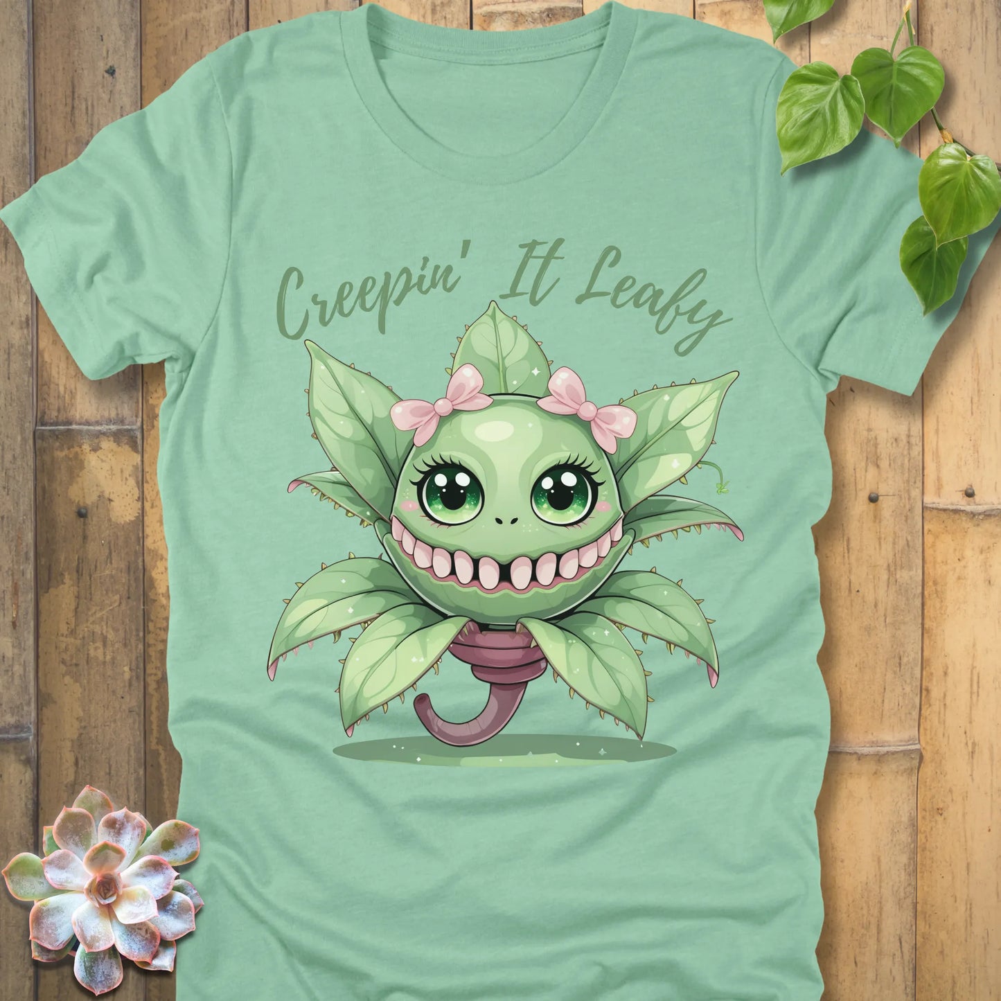 Heather Mint t-shirt featuring the design Creepin' It Leafy printed in green letters and a happy plant