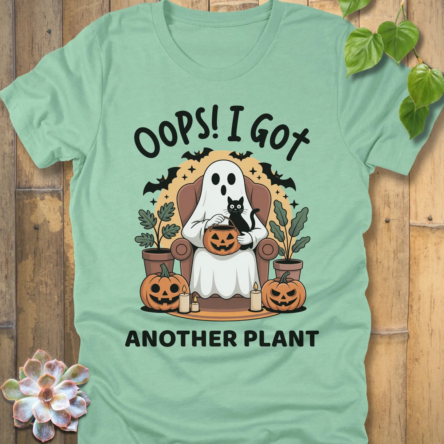 Heather Mint t-shirt featuring the design "Oops! I Got Another Plant" printed in bold black letters, and a ghost, cat, plants, bats and pumpkin