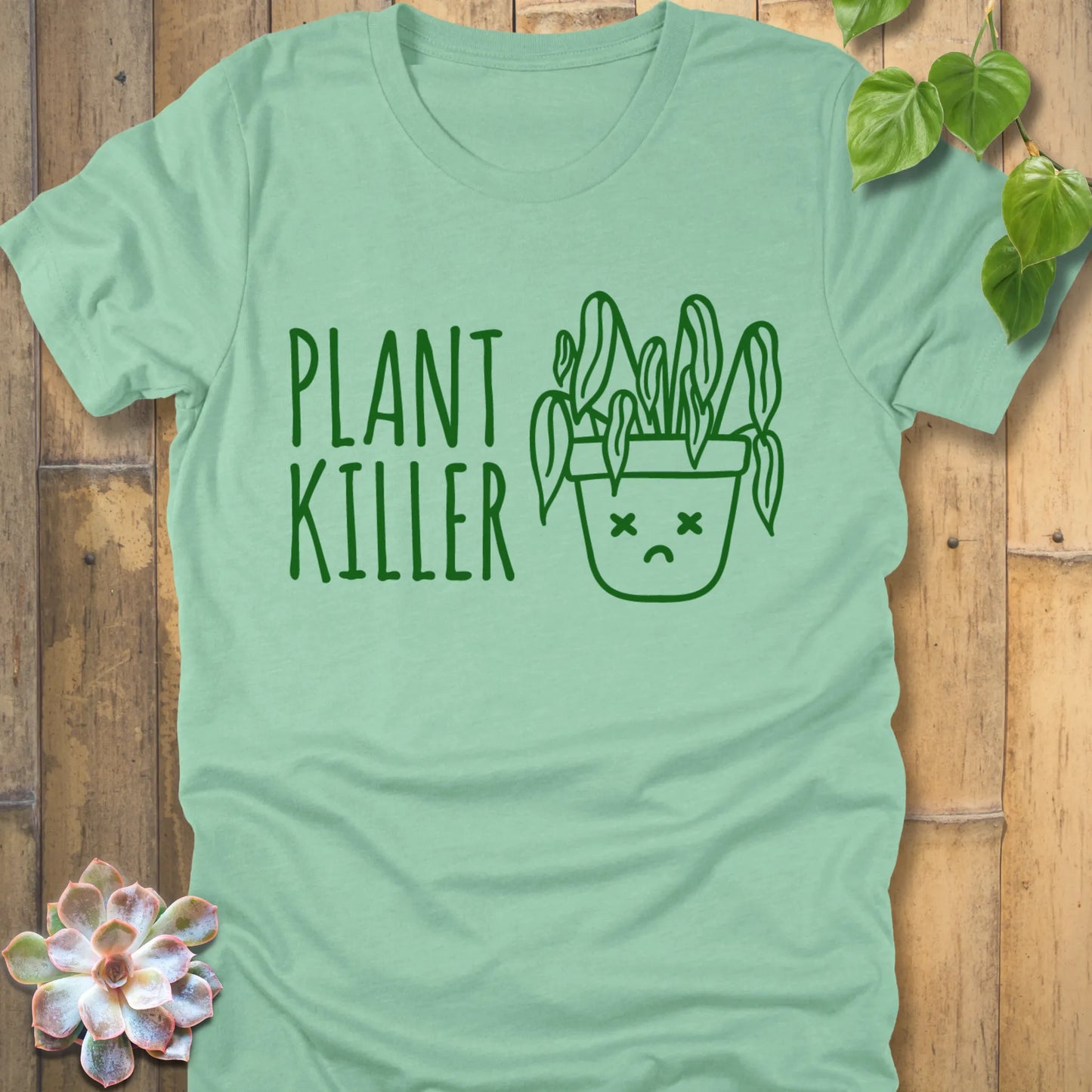 Heather Mint t-shirt featuring the design Plant Killer printed in green letters with a plant in an emoji pot 