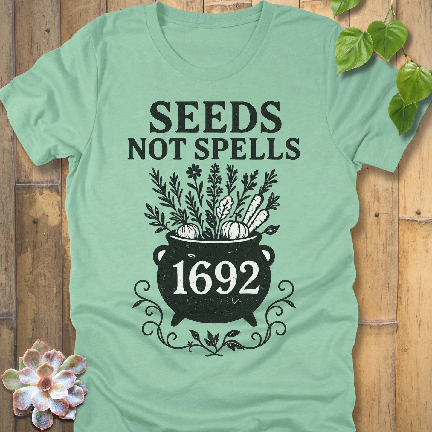 Heather Mint t-shirt featuring the design Seeds Not Spells printed in bold black letters, halloween gardening graphic tee.