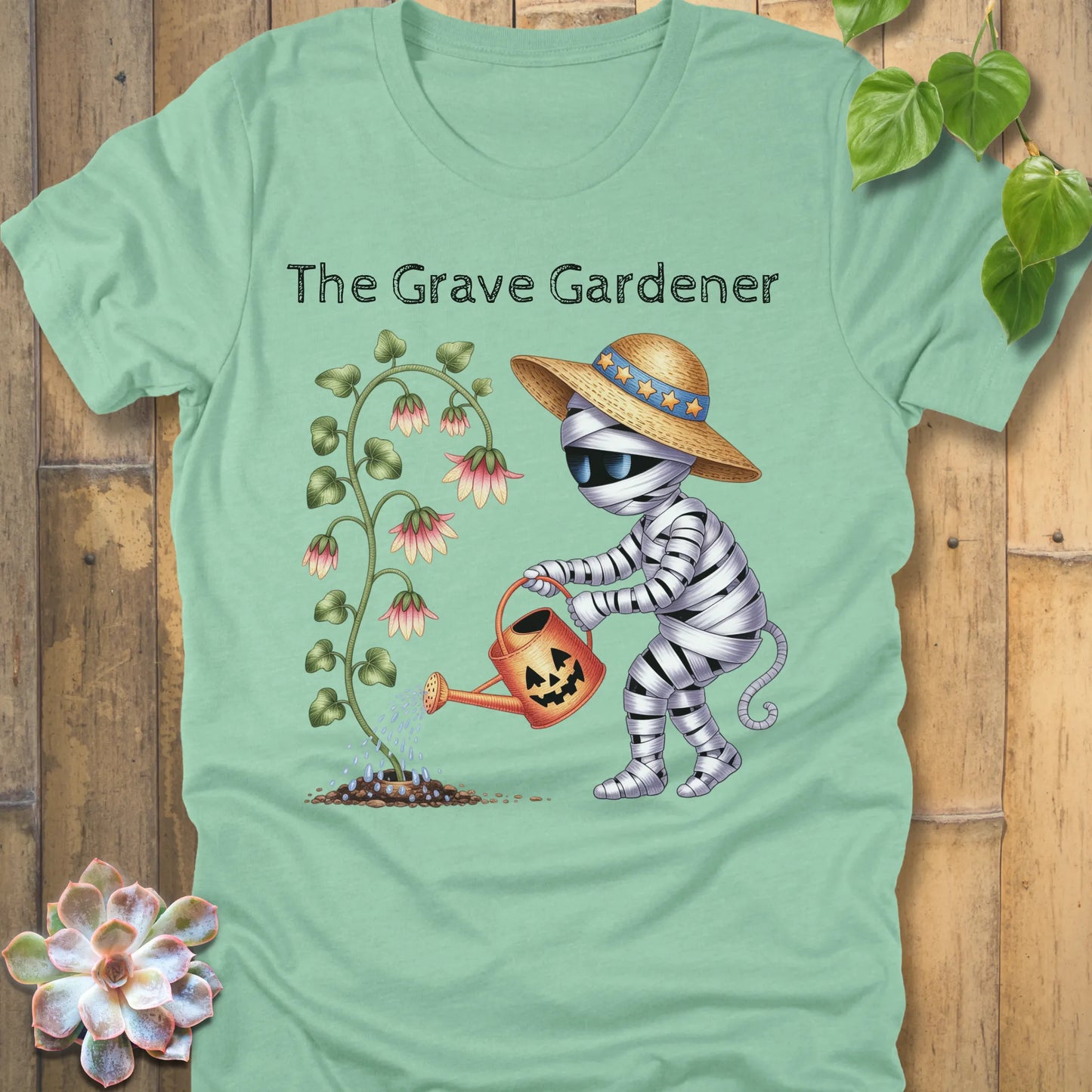 Heather Mint t-shirt featuring the design The Grave Gardener printed in bold black letters and a ghost watering the plant