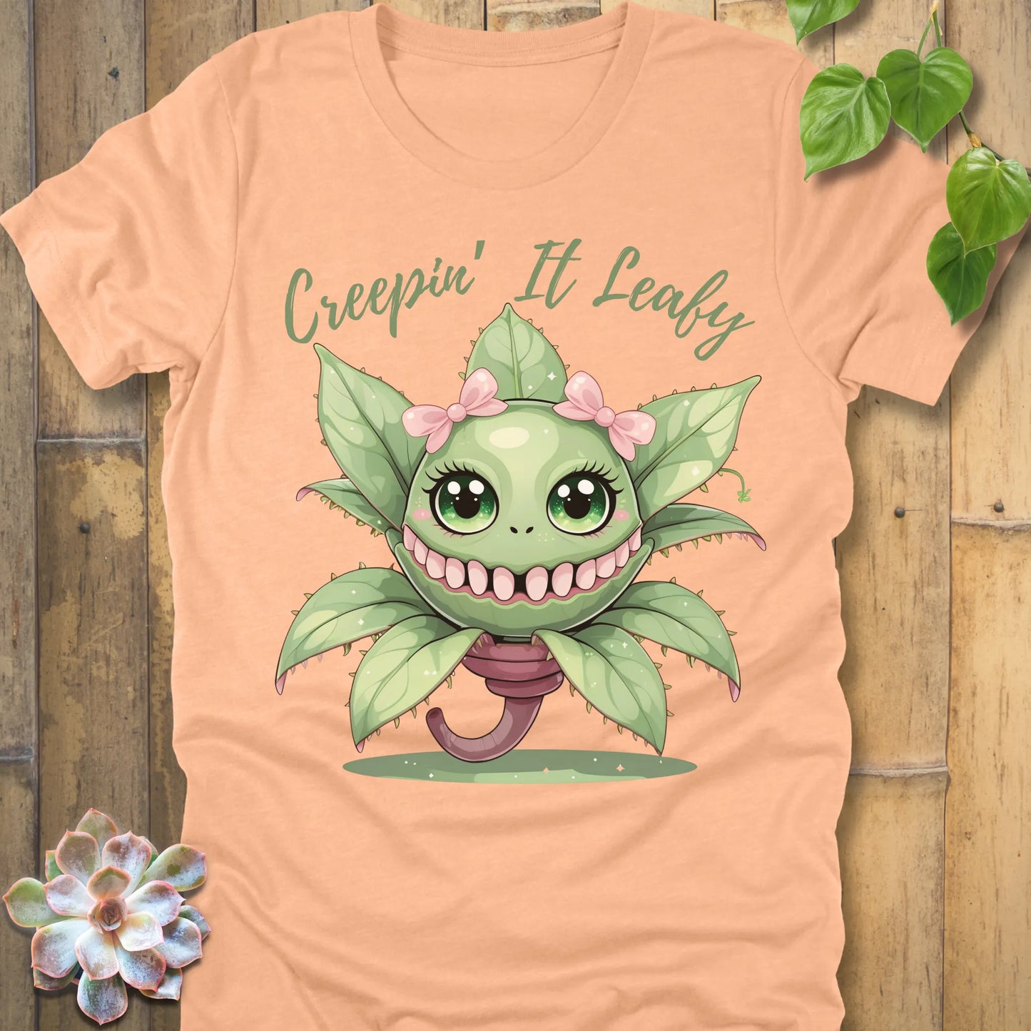 Heather Peach t-shirt featuring the design Creepin' It Leafy printed in green letters and a happy plant