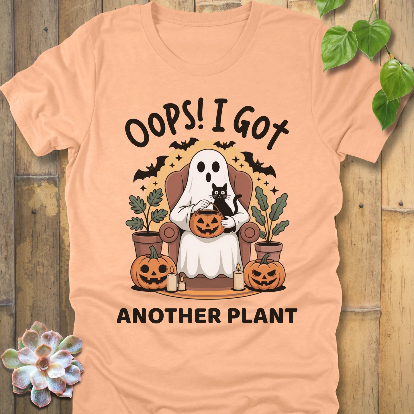 Heather Peach t-shirt featuring the design "Oops! I Got Another Plant" printed in bold black letters, and a ghost, cat, plants, bats and pumpkin