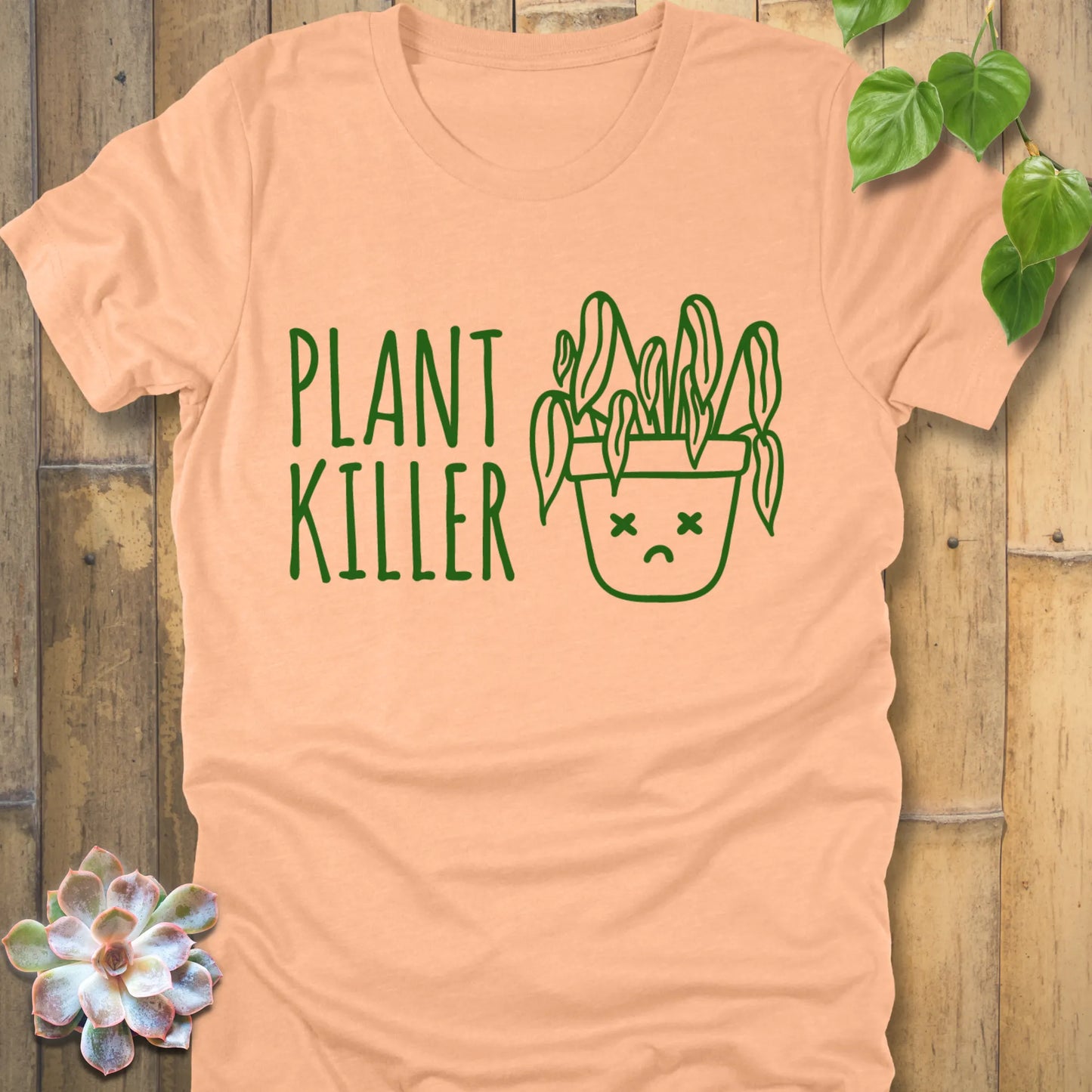 Heather Peach t-shirt featuring the design Plant Killer printed in green letters with a plant in an emoji pot 