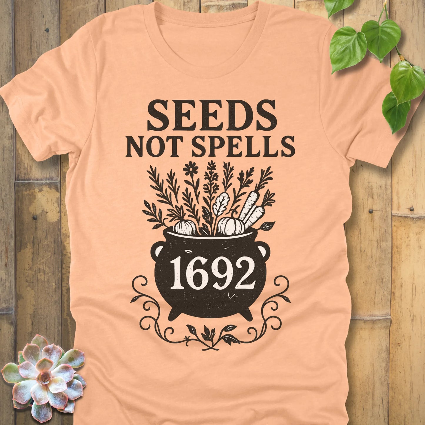 Heather Peach t-shirt featuring the design Seeds Not Spells printed in bold black letters, halloween gardening graphic tee.