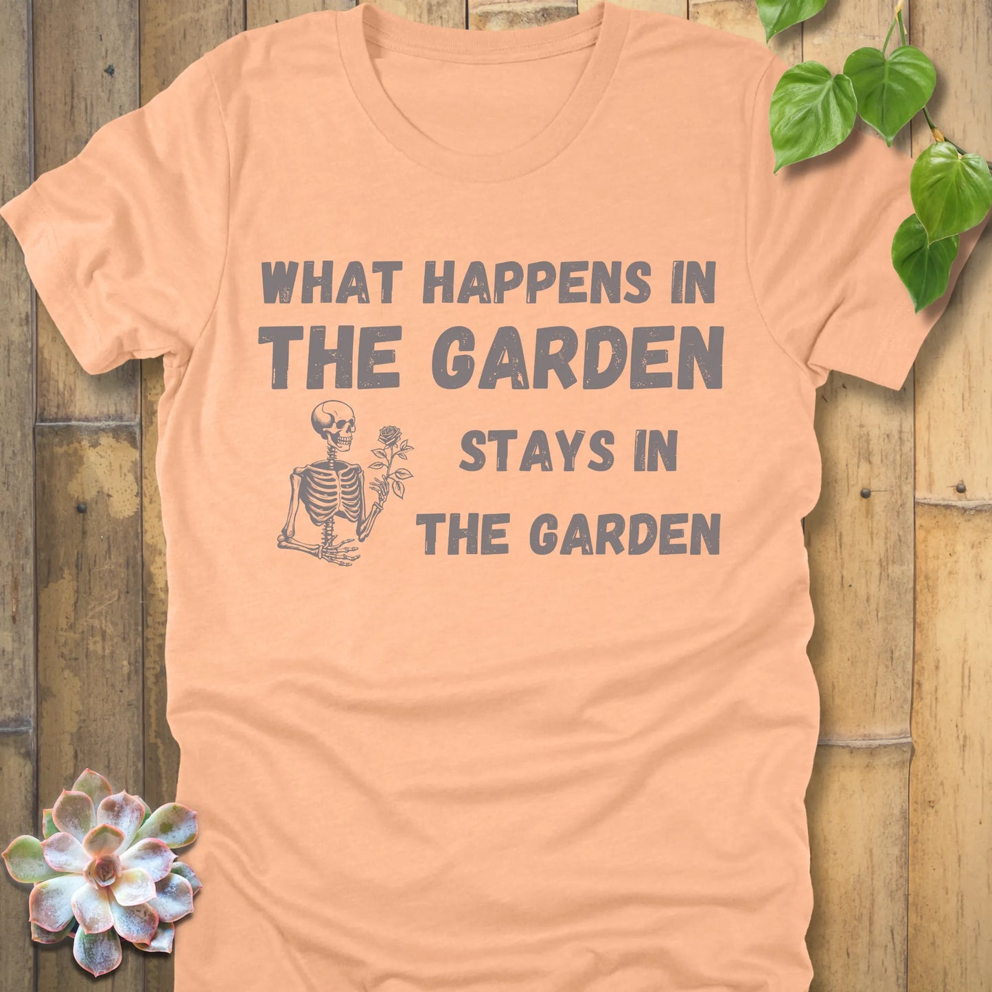 Heather Peach t-shirt featuring the design What Happens In The Garden Stays In The Garden printed in bold letters with skeleton and flower