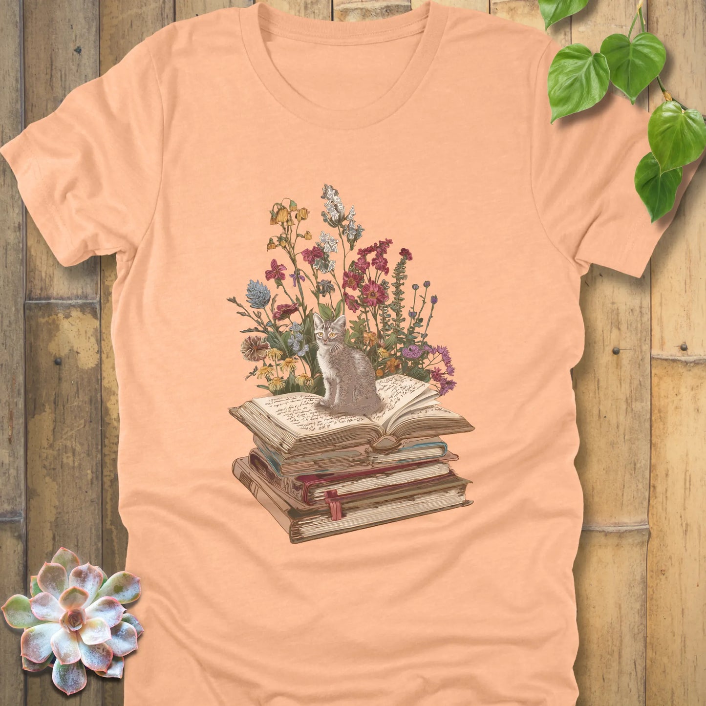 Heather Peack t-shirt featuring the design Whiskers & Words with a cat sitting on books and flowers, eco-style tee for book and cat lovers.