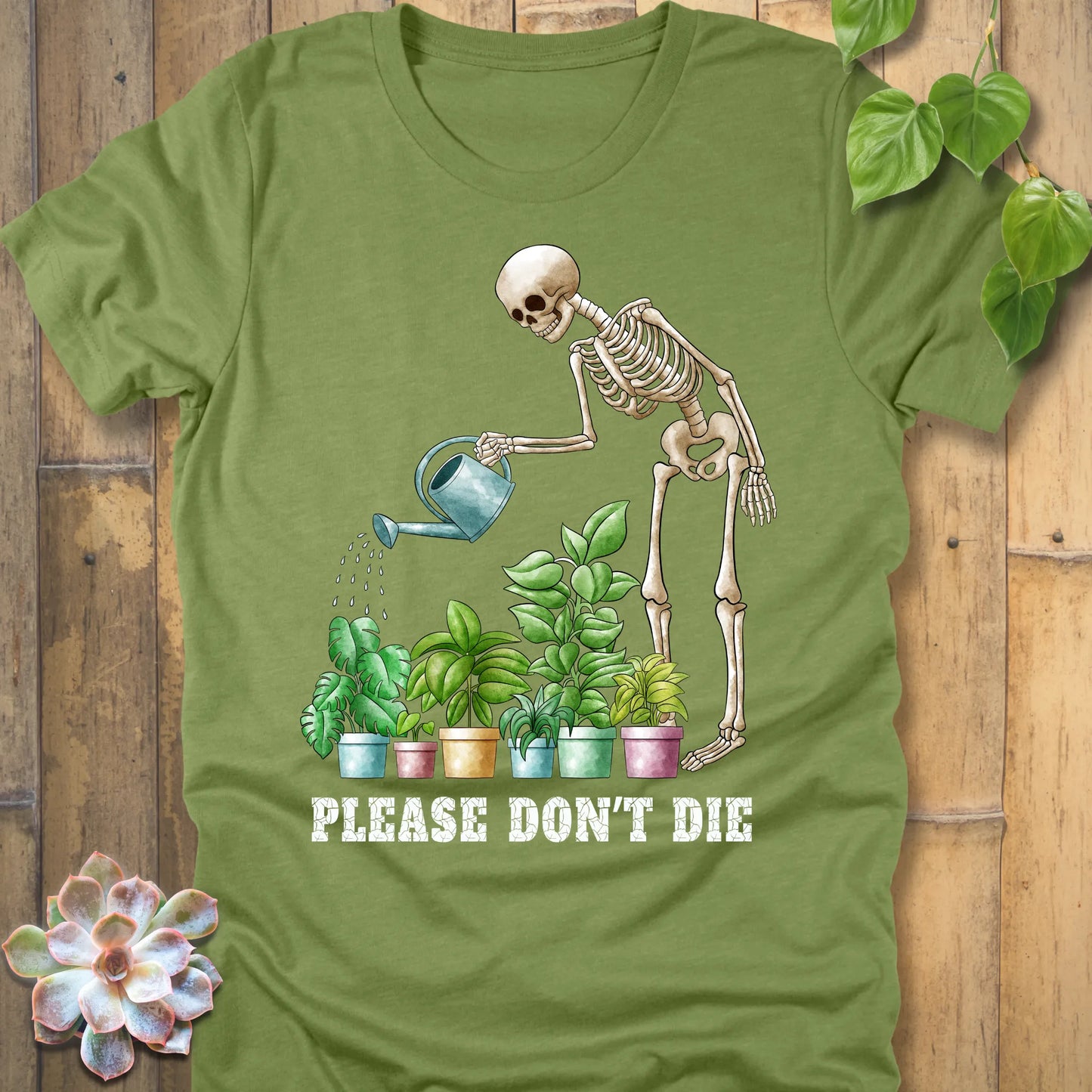 Heather green t-shirt featuring the design Please Don’t Die with skeleton watering plants print