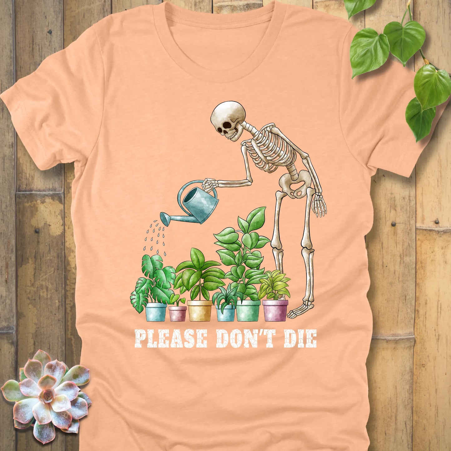 Heather peach t-shirt featuring the design Please Don’t Die with skeleton watering plants print